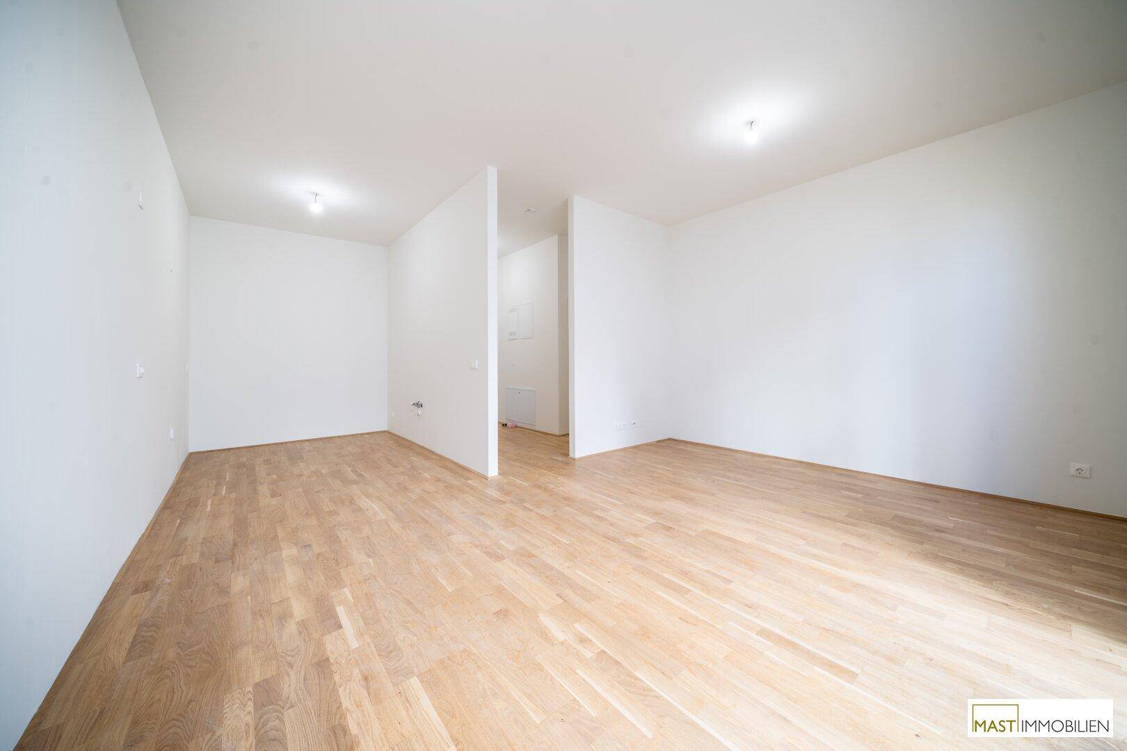 Heller, offener Raum mit Holzboden und weißen Wänden, der vielseitige Nutzungsmöglichkeiten bietet.