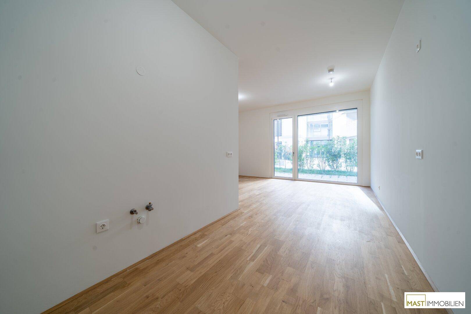 Leerer Raum mit Parkettboden und Anschlüssen an der Wand, ideal für eine Küche oder Hauswirtschaftsraum.