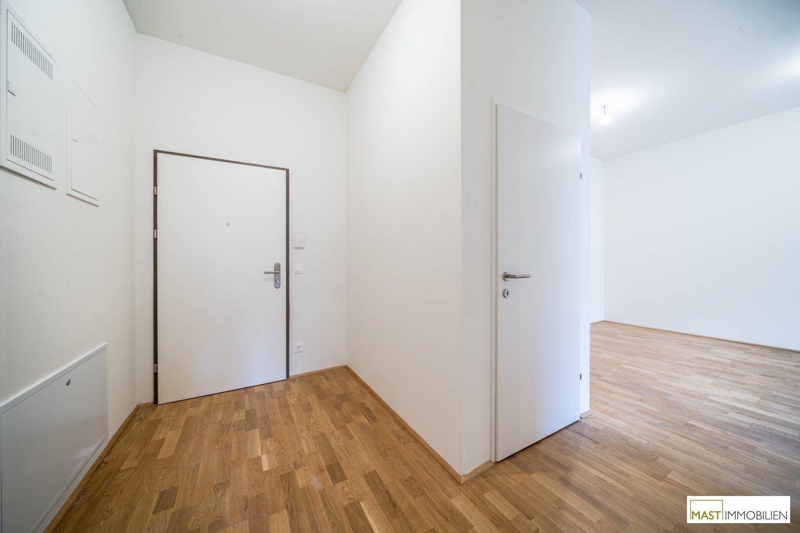 Moderner Eingangsbereich mit hellem Holzboden und zwei weißen Türen, die zu den Zimmern führen.