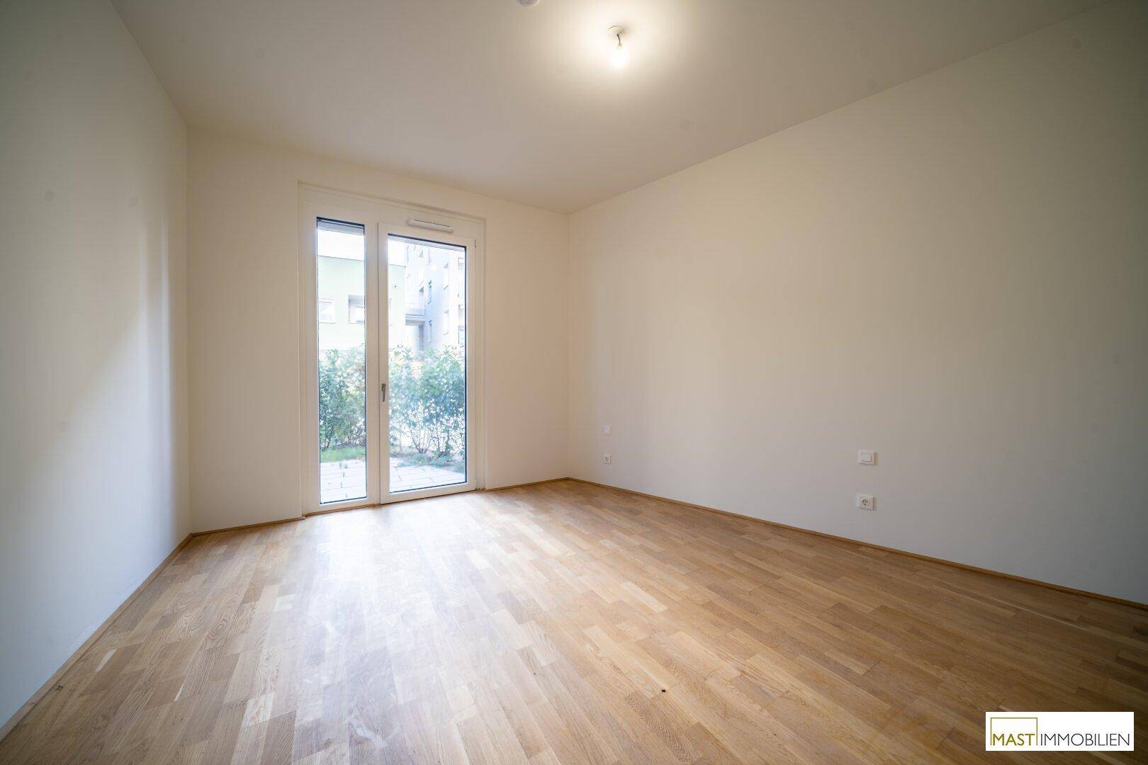 Lichtdurchflutetes Zimmer mit Holzboden und einer Glastür, die den direkten Zugang zum Garten ermöglicht.
