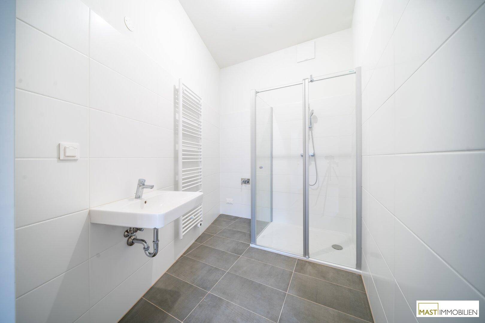 Modernes Badezimmer mit weißen Wandfliesen, grauen Bodenfliesen, einer Duschkabine und einem beheizten Handtuchhalter.