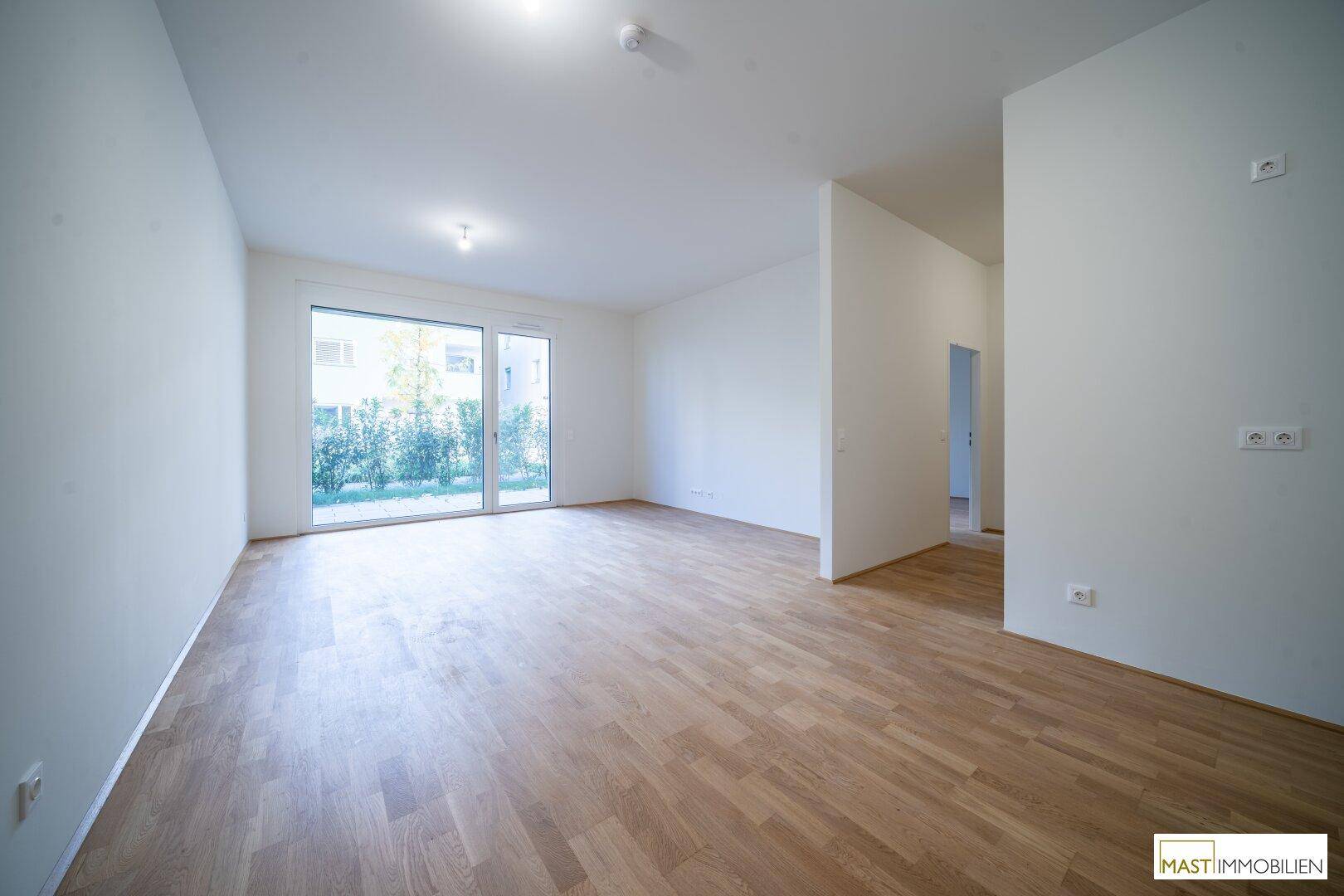Heller Wohnbereich mit Holzboden und großen Fenstern, die Zugang zu einem begrünten Außenbereich bieten.