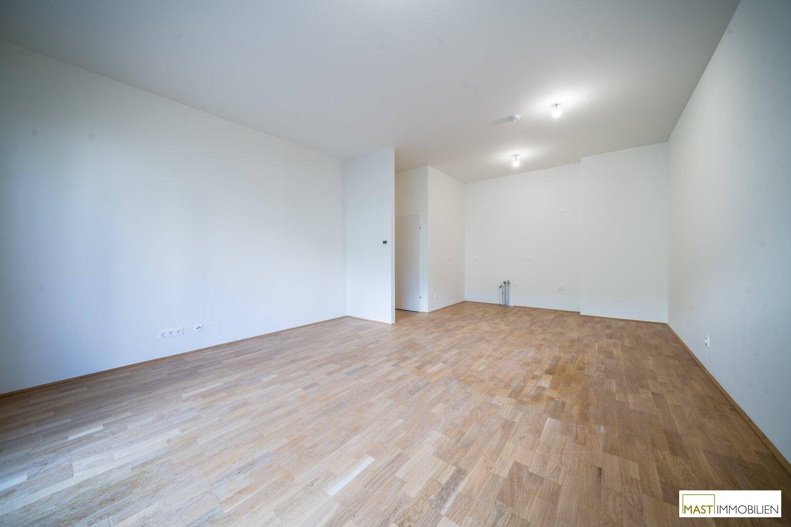 Leerer Raum mit Holzboden und weißen Wänden, vorbereitet für die Installation einer Küche oder eines Hauswirtschaftsraums.
