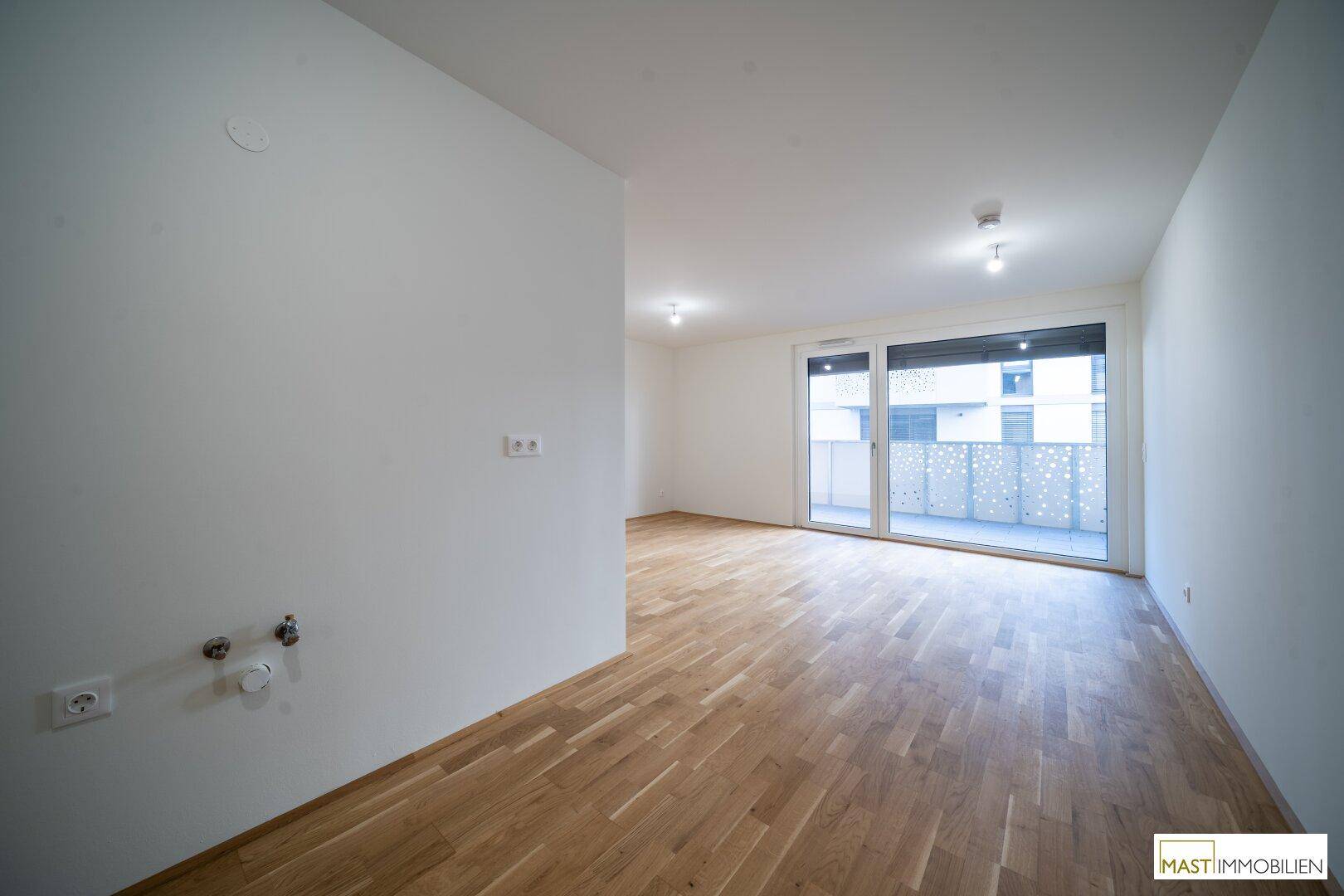 Heller Wohnraum mit Parkettboden und Zugang zu einem Balkon oder einer Terrasse.