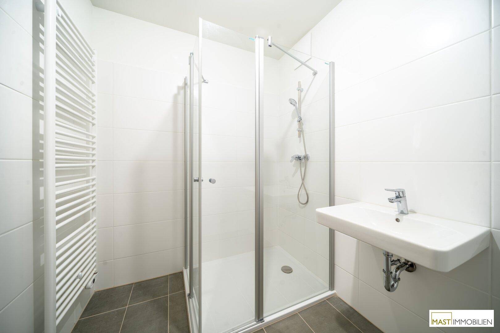 Modernes Badezimmer mit weißen Fliesen, Duschkabine, Waschbecken und Handtuchheizkörper.