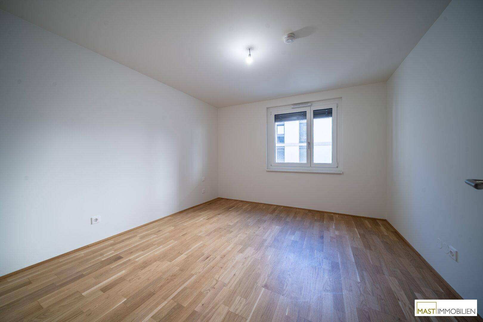 Helles Schlafzimmer mit Parkettboden und einem Fenster, bereit zur individuellen Gestaltung.