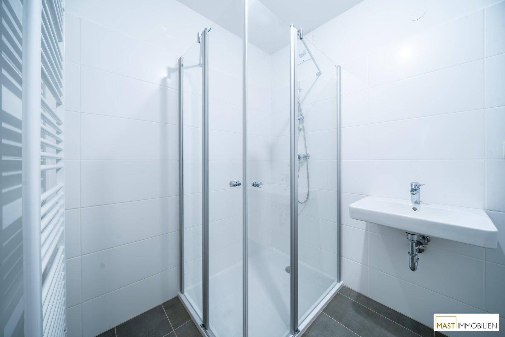 Modernes Badezimmer mit Eckdusche, Waschbecken und beheiztem Handtuchhalter.