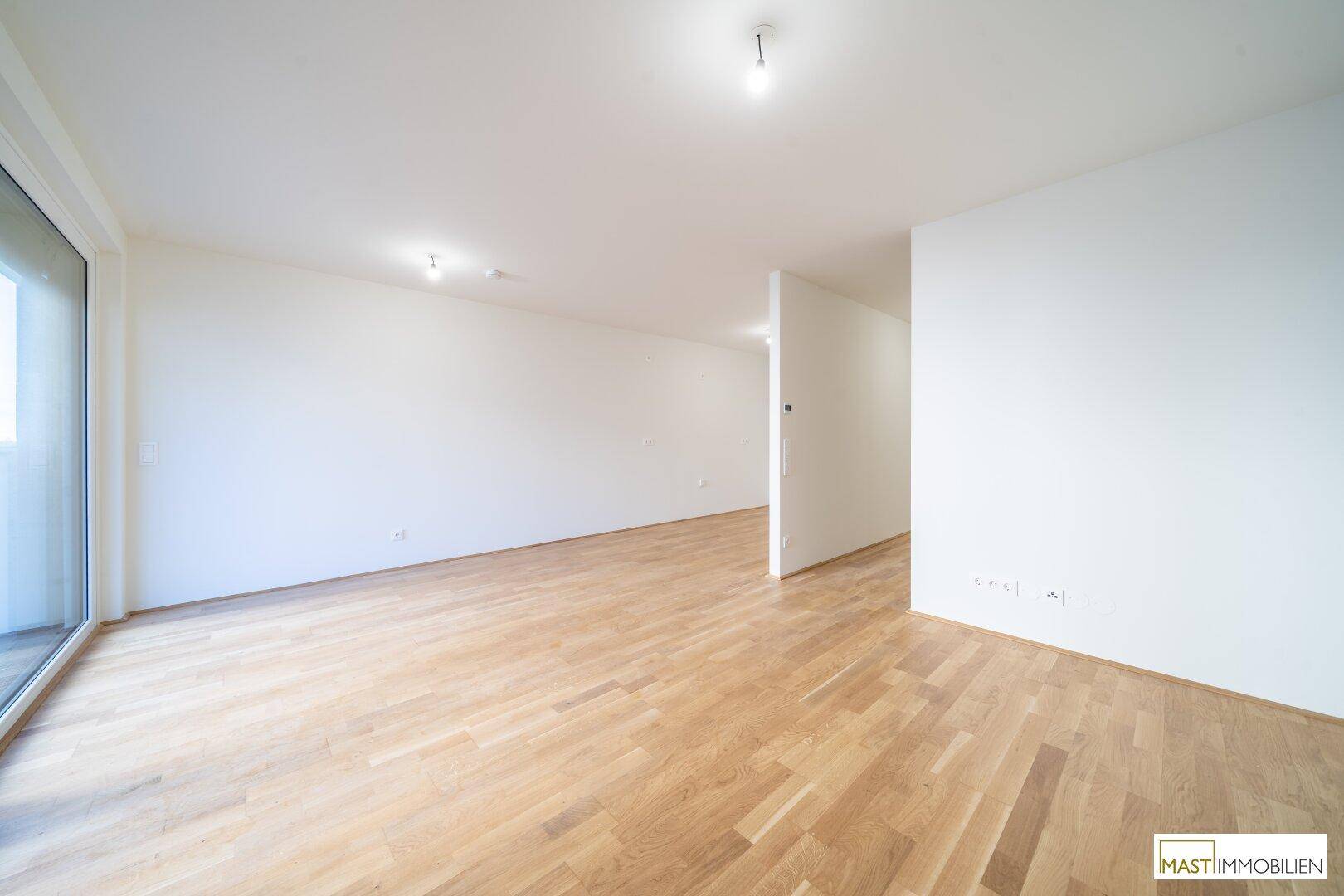 Heller, leerer Wohnbereich mit modernem Parkettboden und Zugang zu einem Balkon.