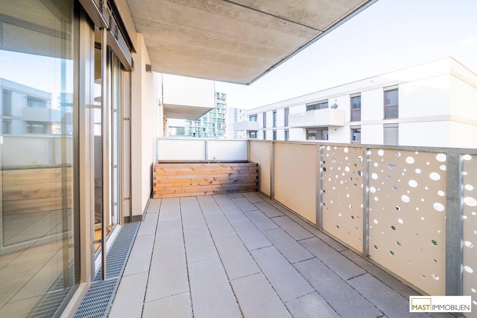 Moderner Balkon mit Fliesenboden, perforiertem Geländer und Blick auf umliegende Gebäude.