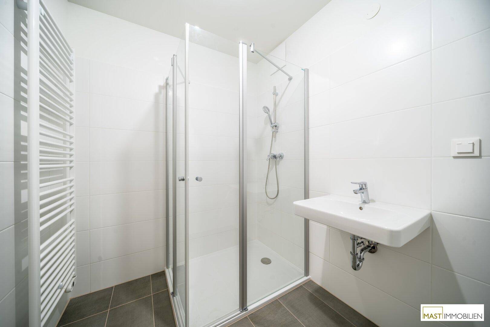 Modernes Badezimmer mit Duschkabine, Waschbecken und beheiztem Handtuchhalter.