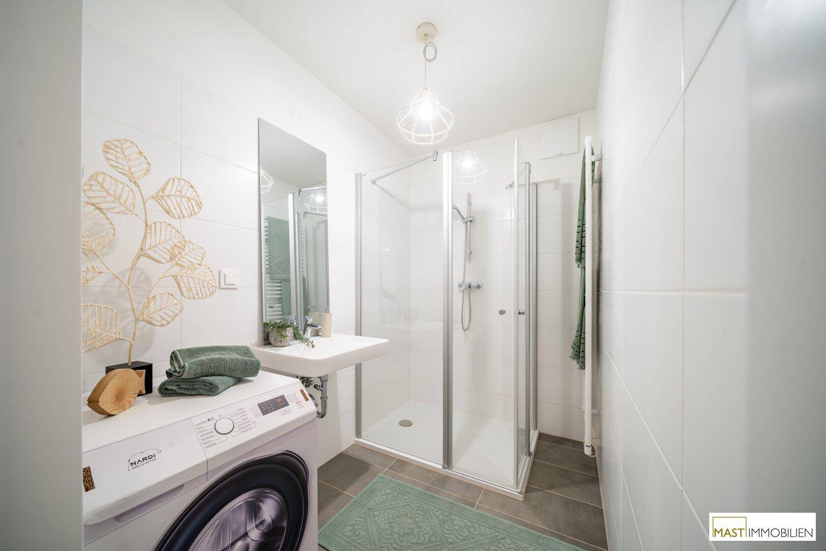 Modernes Badezimmer mit Duschkabine, Waschmaschine und beheiztem Handtuchhalter, hell gefliest.
