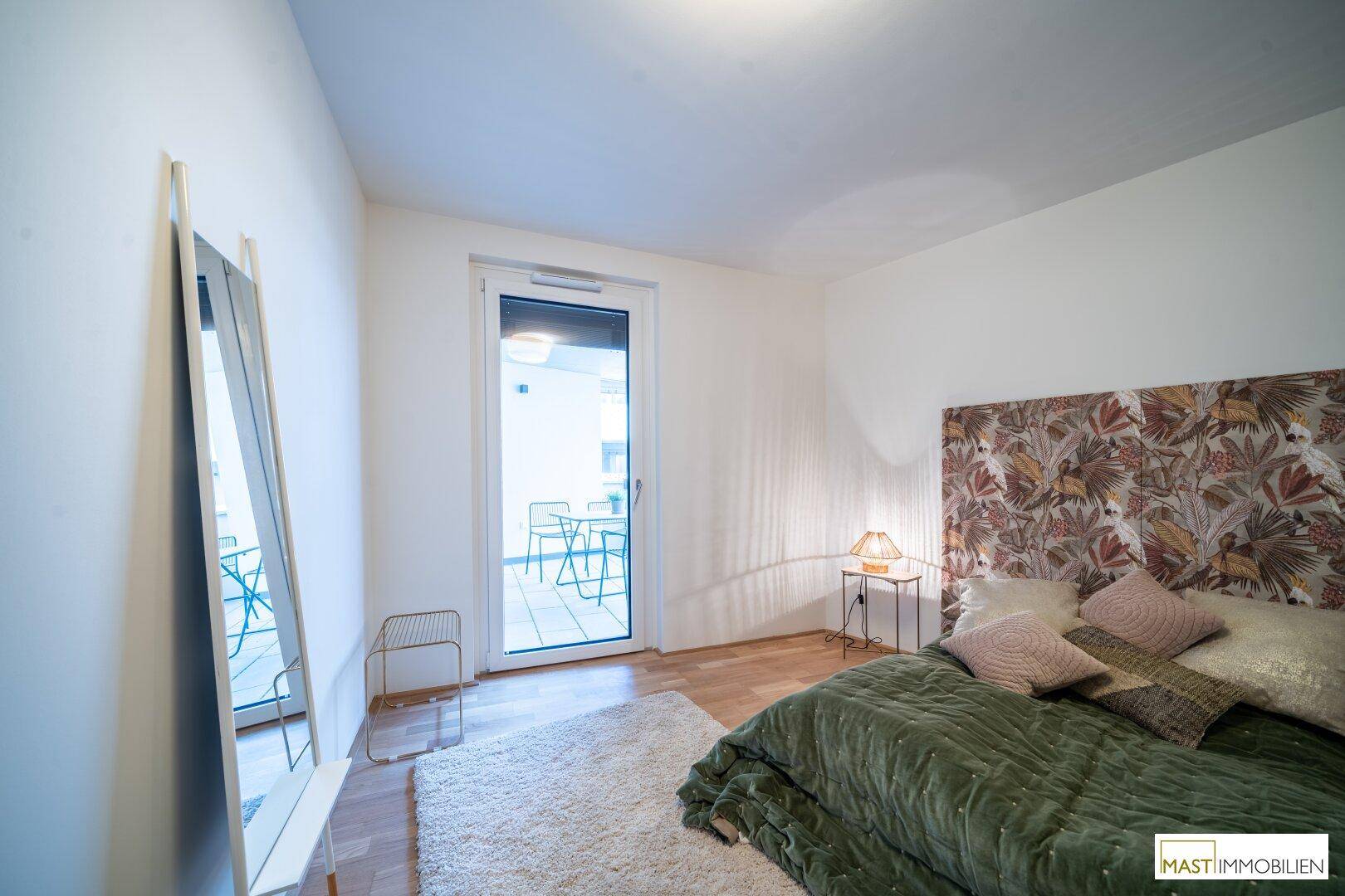 Geräumiges Schlafzimmer mit Holzboden und großem Spiegel, bietet direkten Zugang zum Balkon.