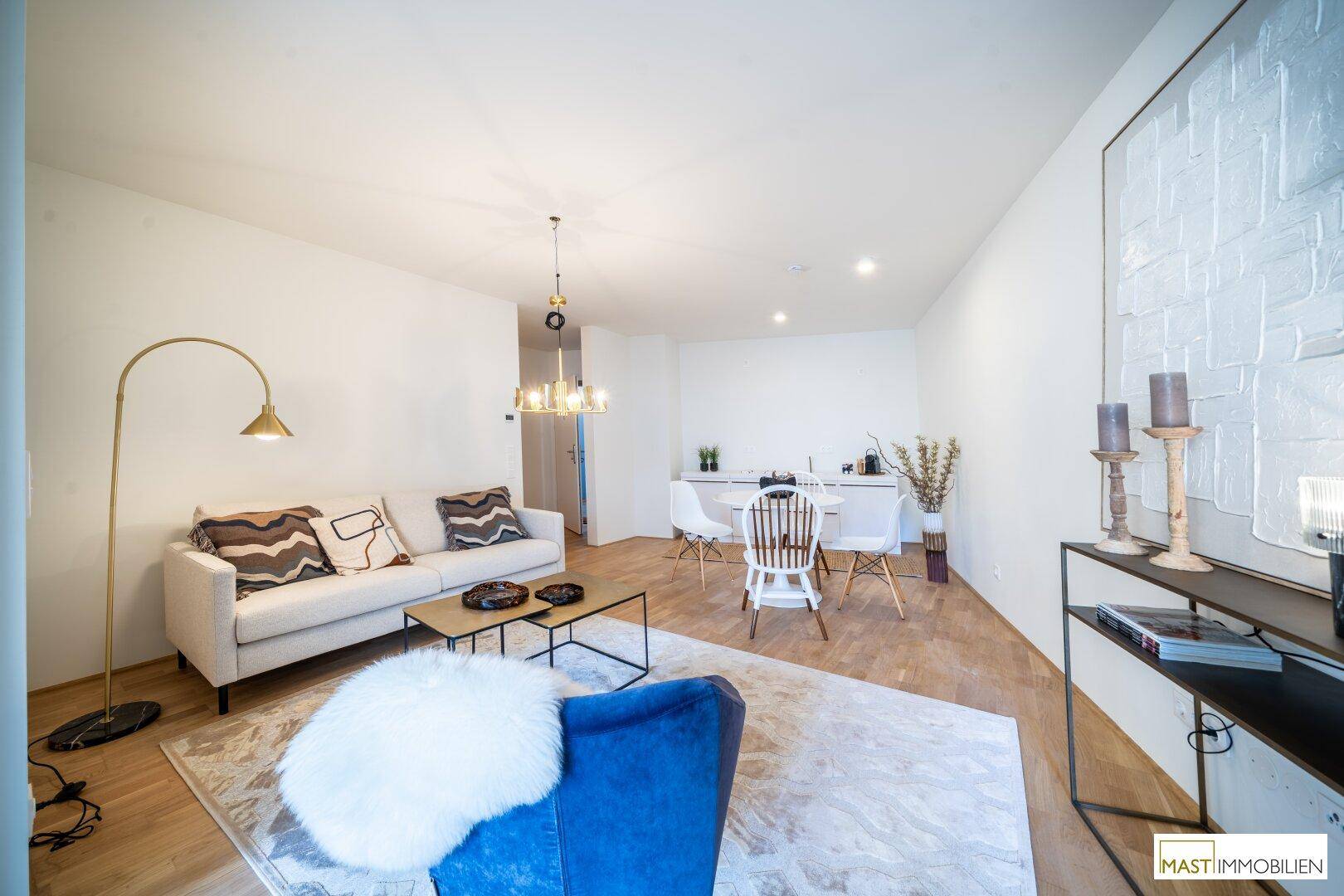 Heller Wohn-Essbereich mit modernem Sofa, blauem Sessel und Essplatz, ergänzt durch eine Küchenzeile.