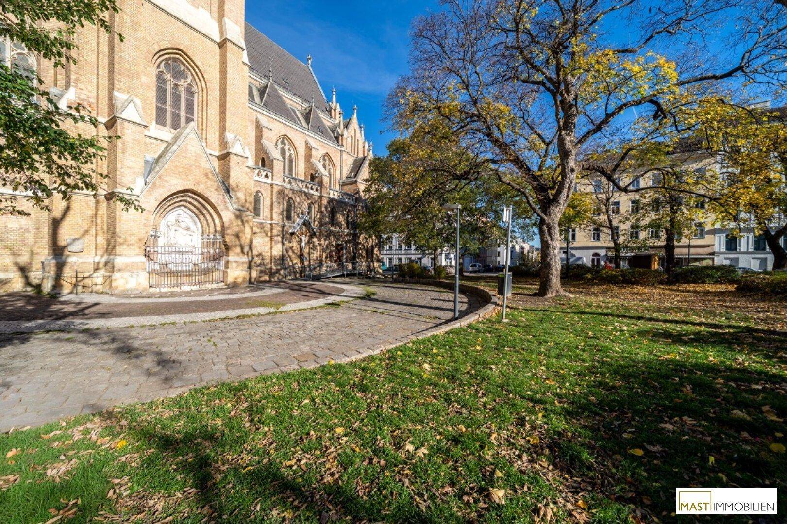 Historische Kirche mit Grünfläche und Bäumen an einem sonnigen Herbsttag.