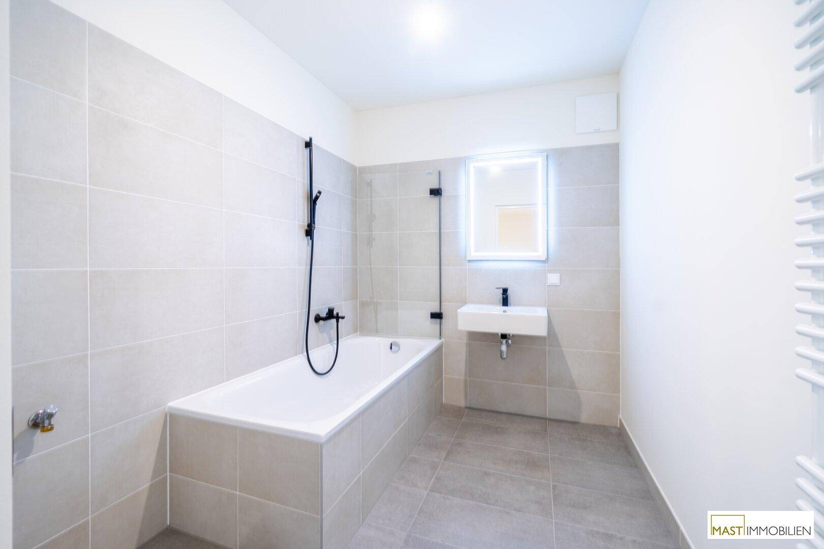 Modernes Badezimmer mit Badewanne, Duscharmatur, Einzelwaschbecken und grauen Fliesen.