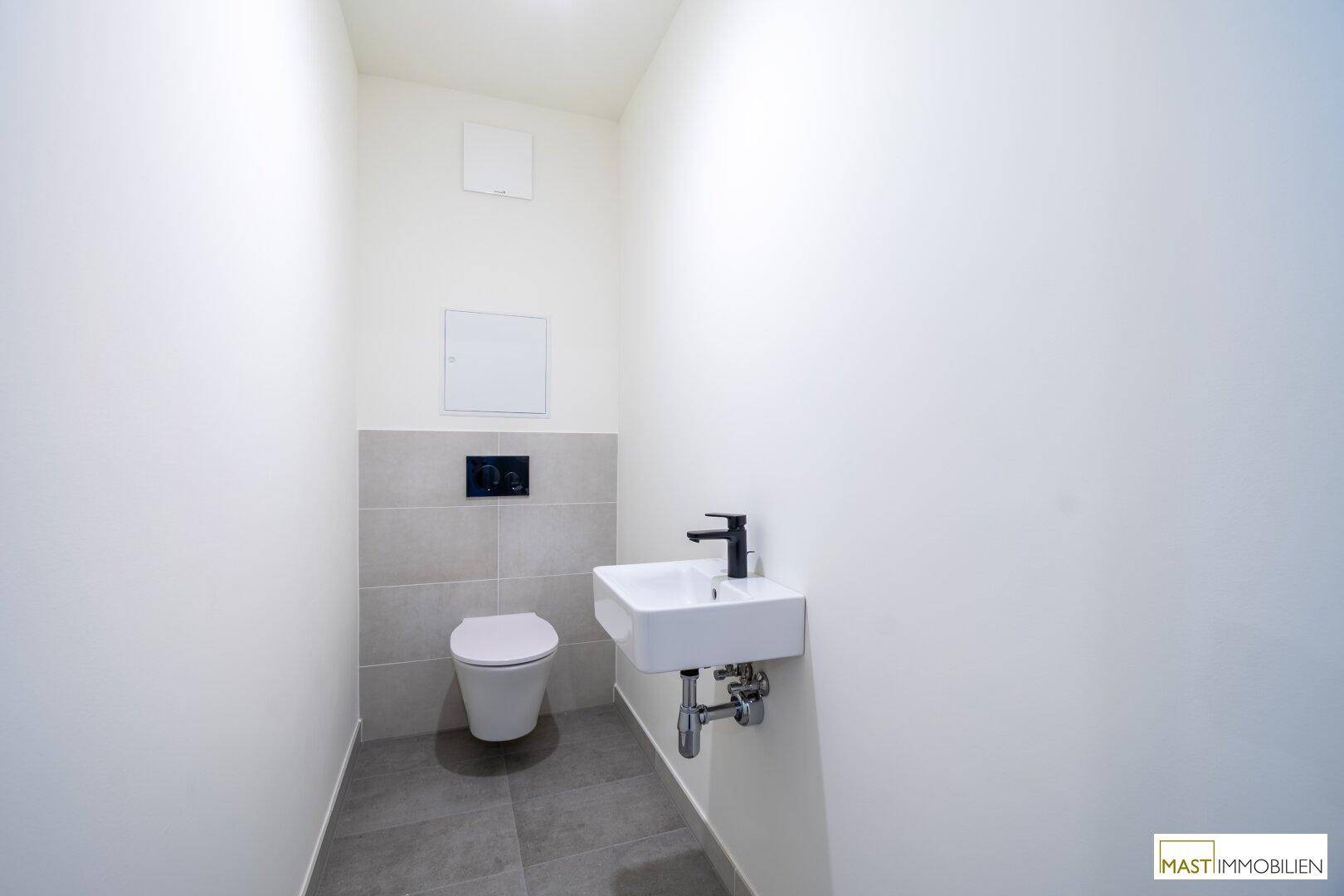 Modernes Gäste-WC mit wandhängendem WC, kleinem Waschbecken und grauen Fliesen.