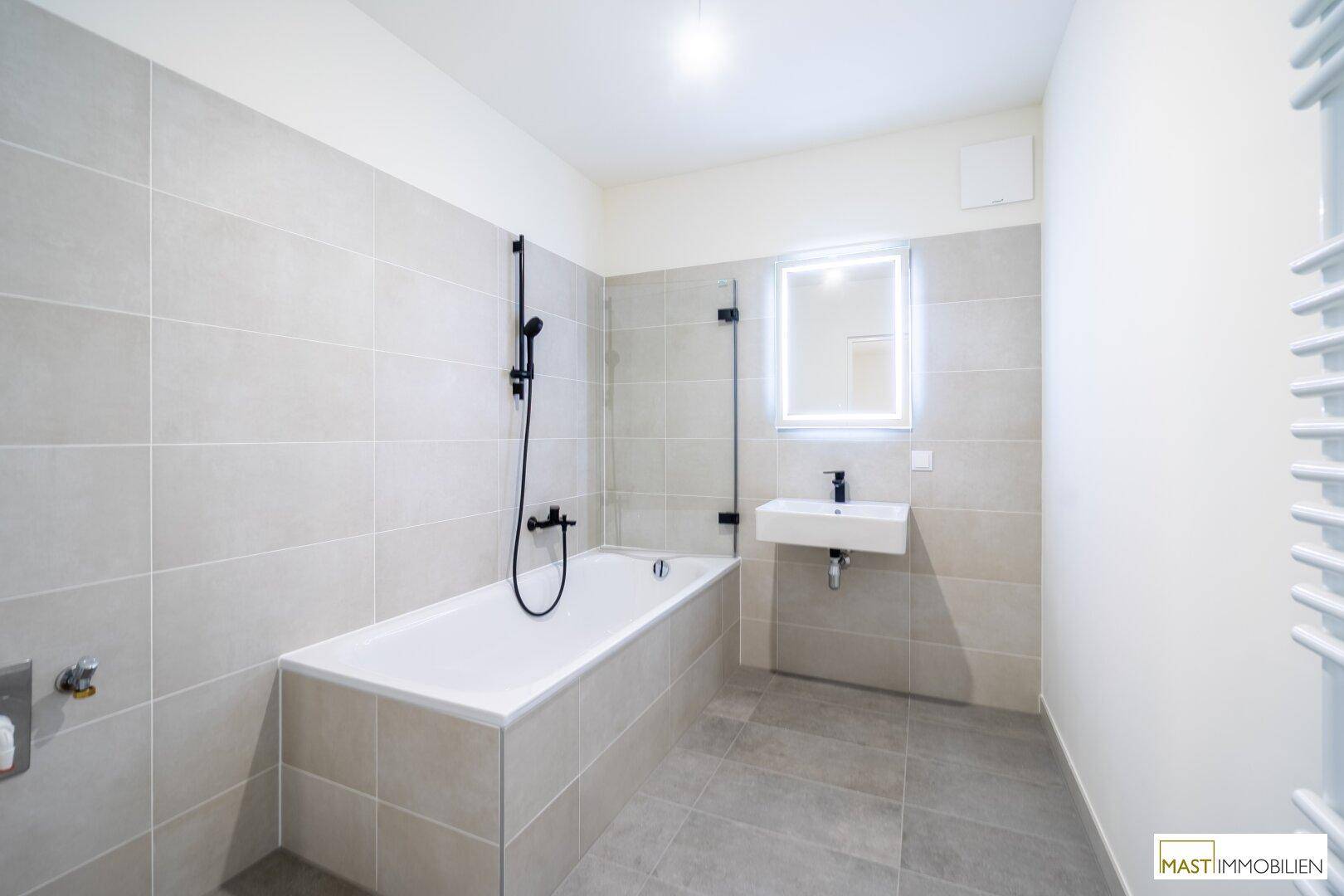Modernes Badezimmer mit Badewanne, Duschfunktion, Waschbecken und beheiztem Handtuchhalter.