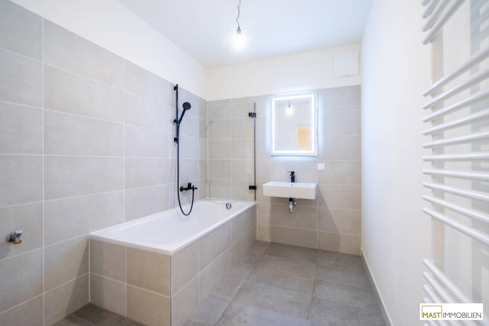 Helles Badezimmer mit Badewanne, Dusche, modernem Waschbecken und beheiztem Handtuchhalter.