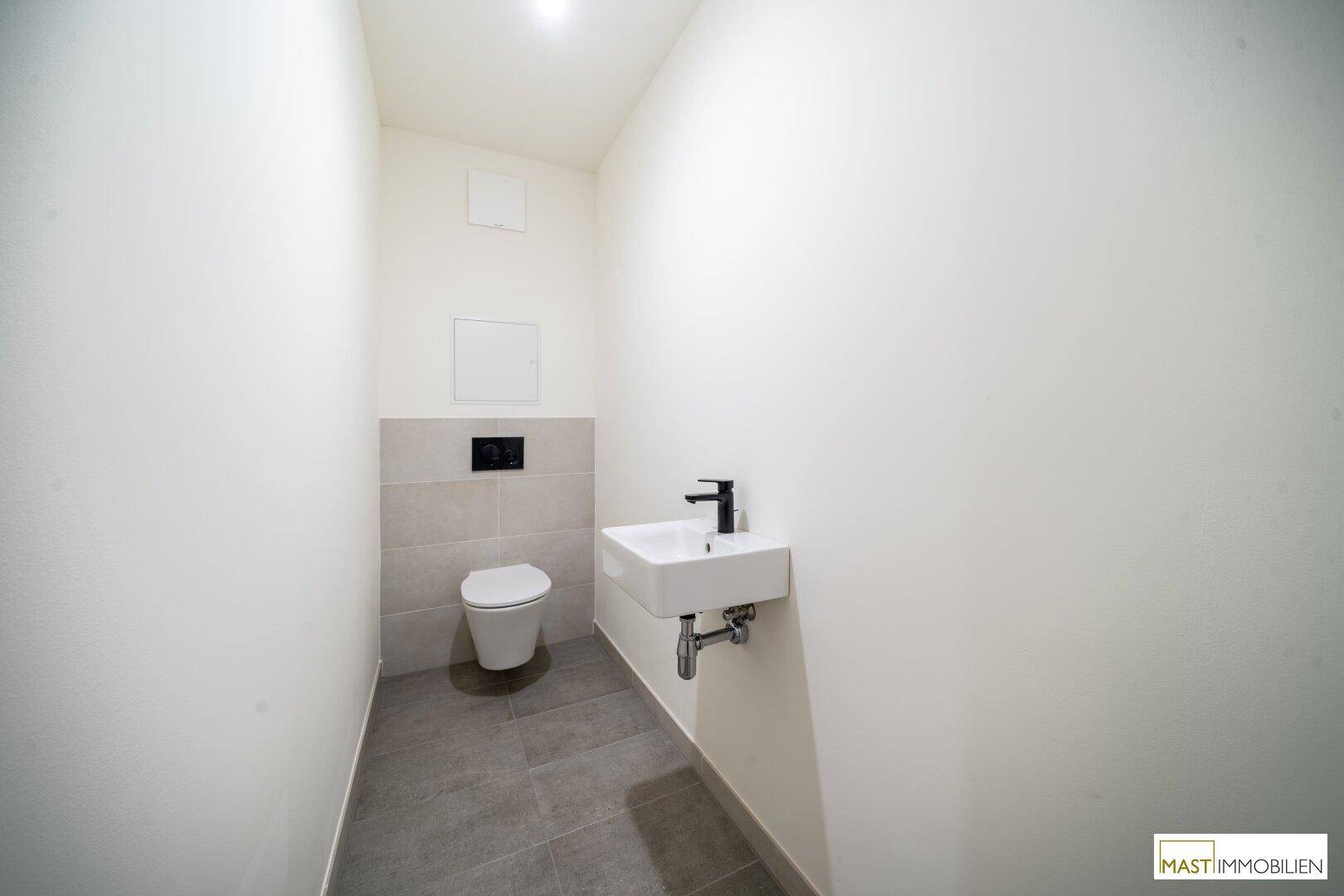 Modernes Gäste-WC mit wandhängendem WC, kleinem Waschbecken und grauen Fliesen.