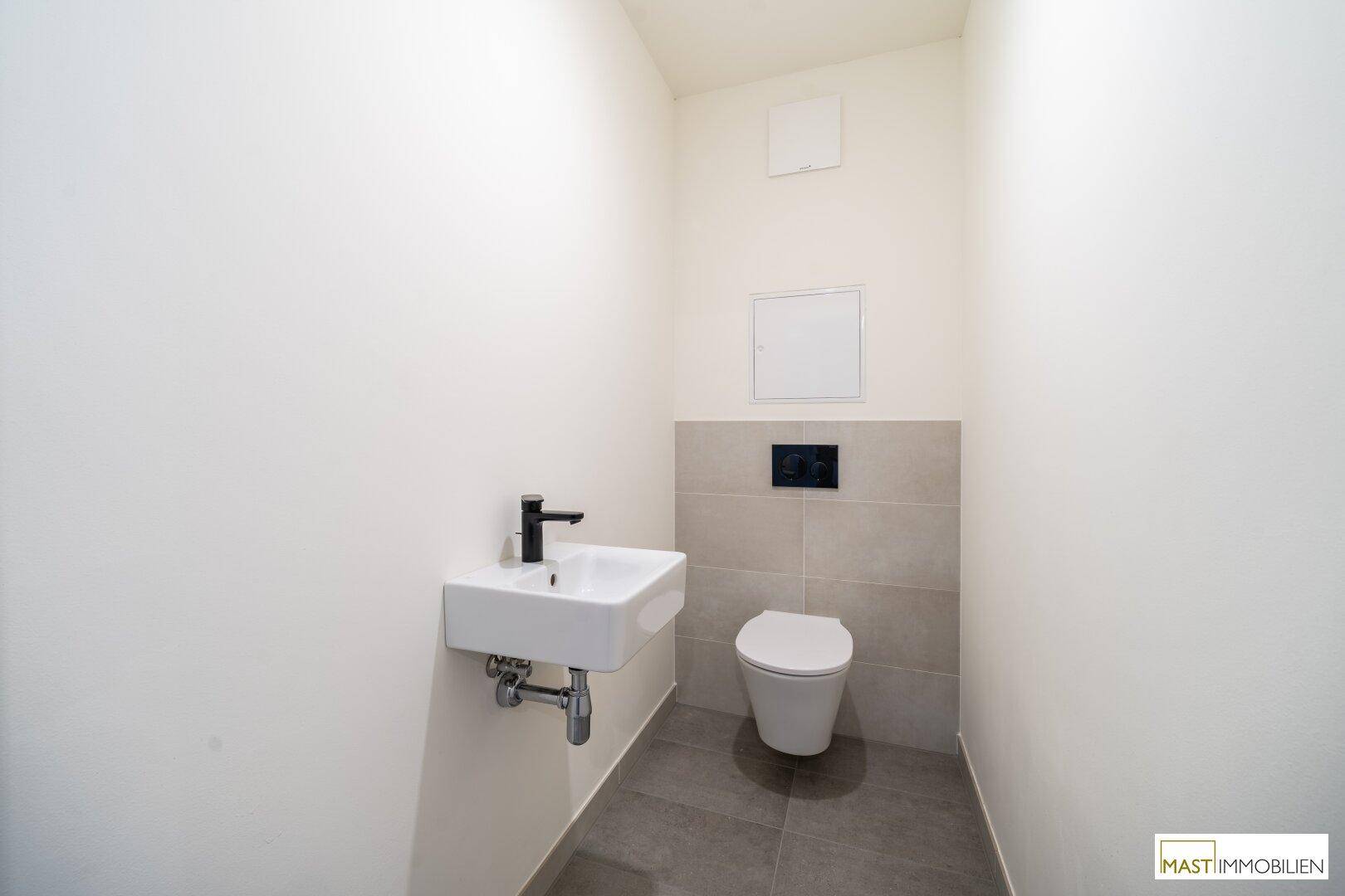 Kleines Gäste-WC mit modernem Wand-WC und Waschbecken, ausgestattet mit grauen Bodenfliesen.