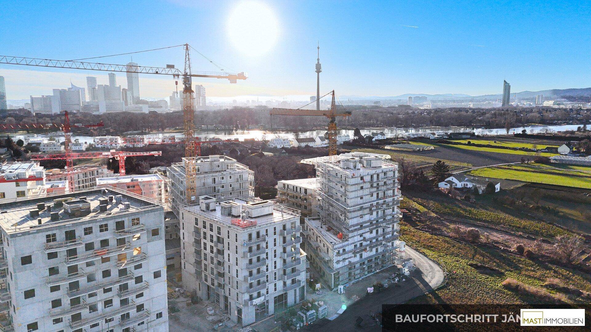 Luftaufnahme einer Baustelle mit mehreren im Bau befindlichen Gebäuden und Stadtpanorama im Hintergrund.