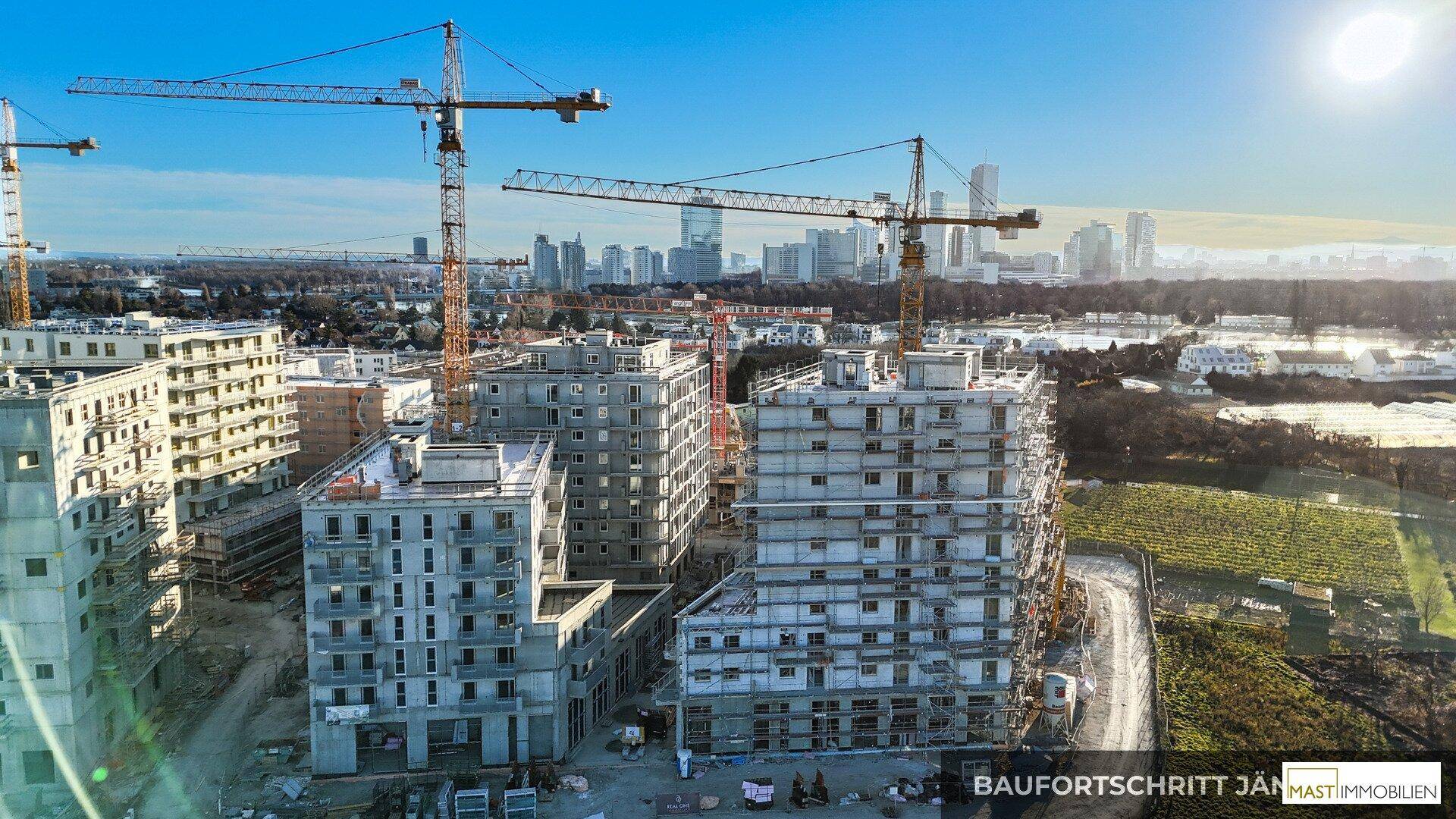 Übersicht der Baufortschritte mit mehreren Gebäudestrukturen, Kränen und der urbanen Landschaft im Hintergrund.