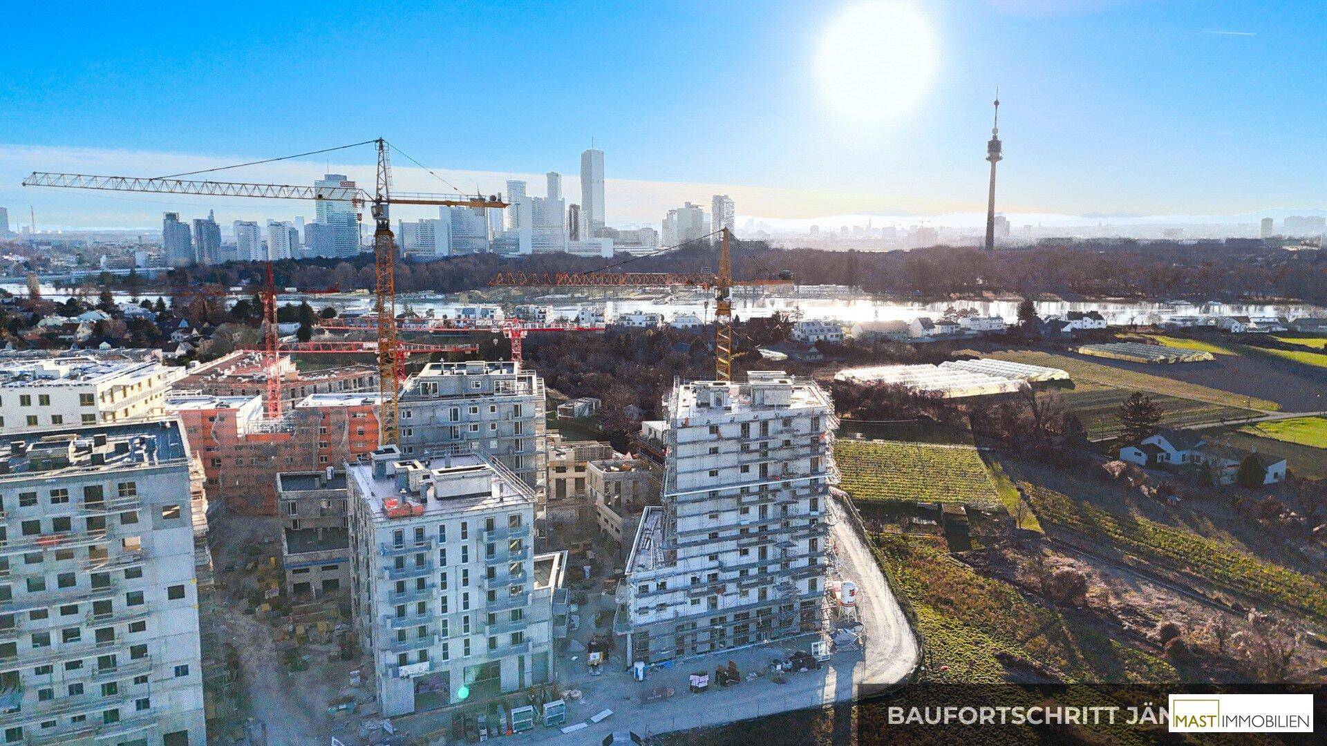 Panoramablick auf eine Baustelle mit entstehenden Wohngebäuden, Kränen und der Stadt Wien in der Ferne.