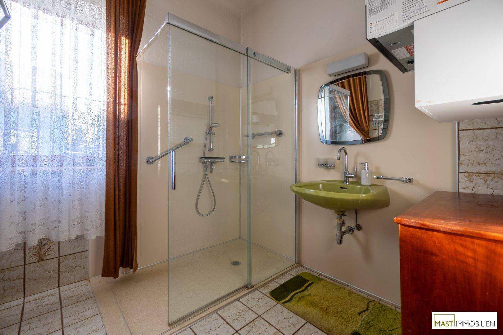 Badezimmer mit Dusche, grünem Waschbecken und Fenster.
