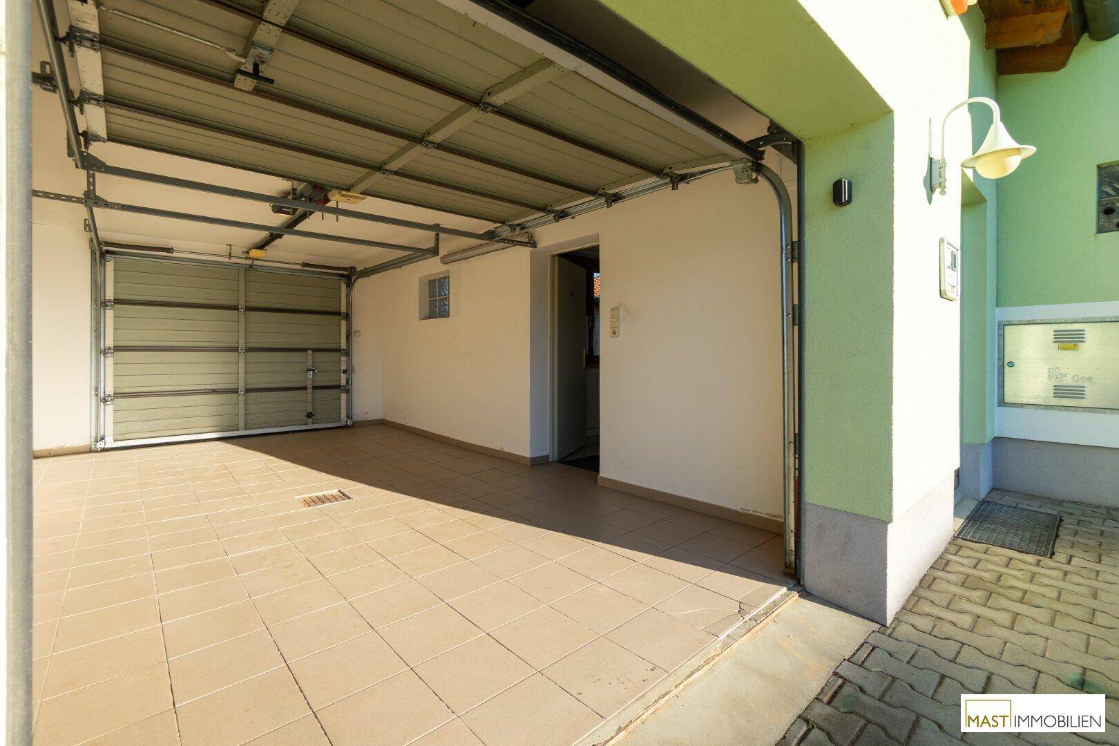 Geräumige Garage mit Fliesenboden und offenem Garagentor.