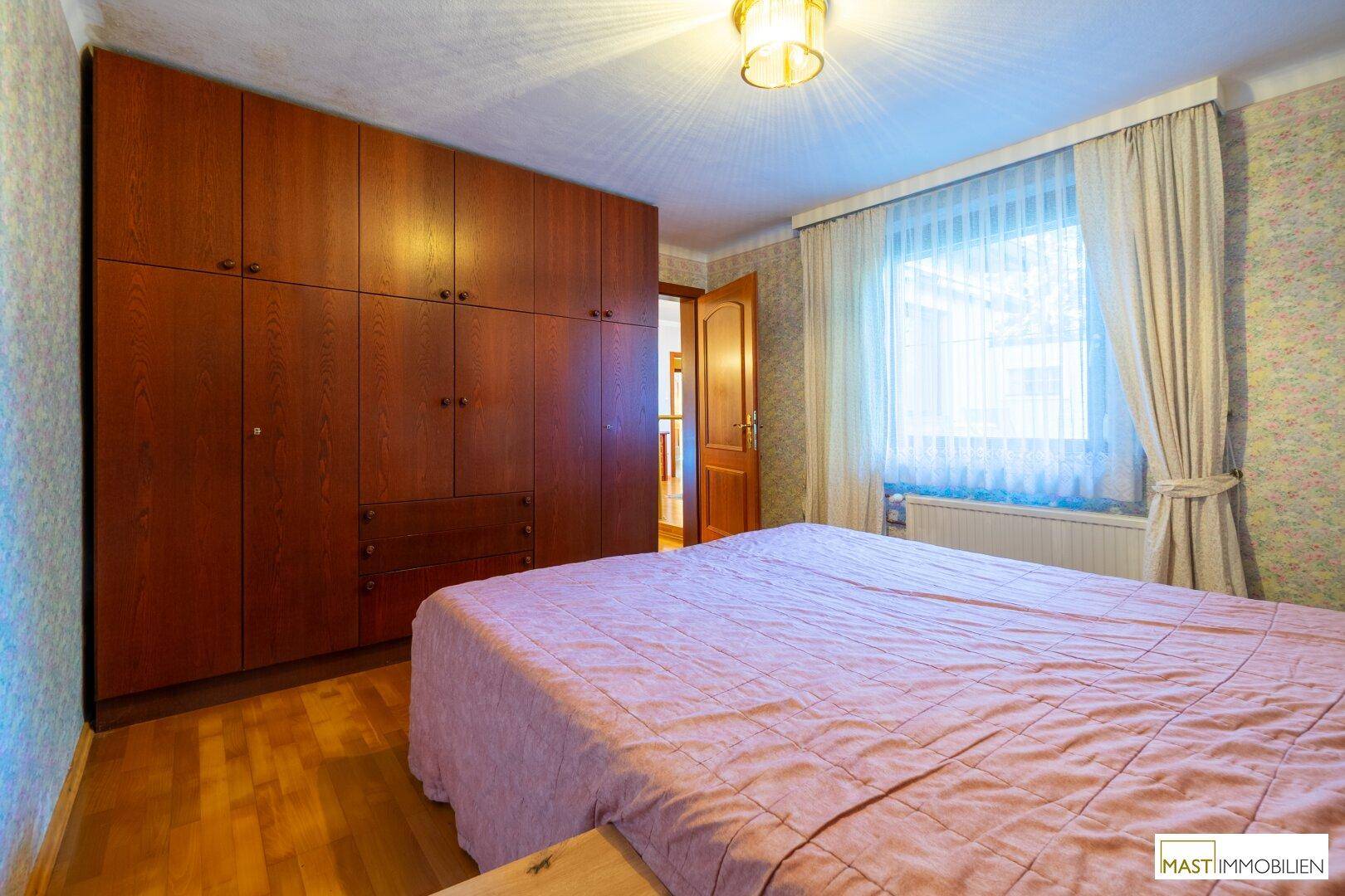 Schlafzimmer mit großem Einbauschrank, Doppelbett und Fenster.