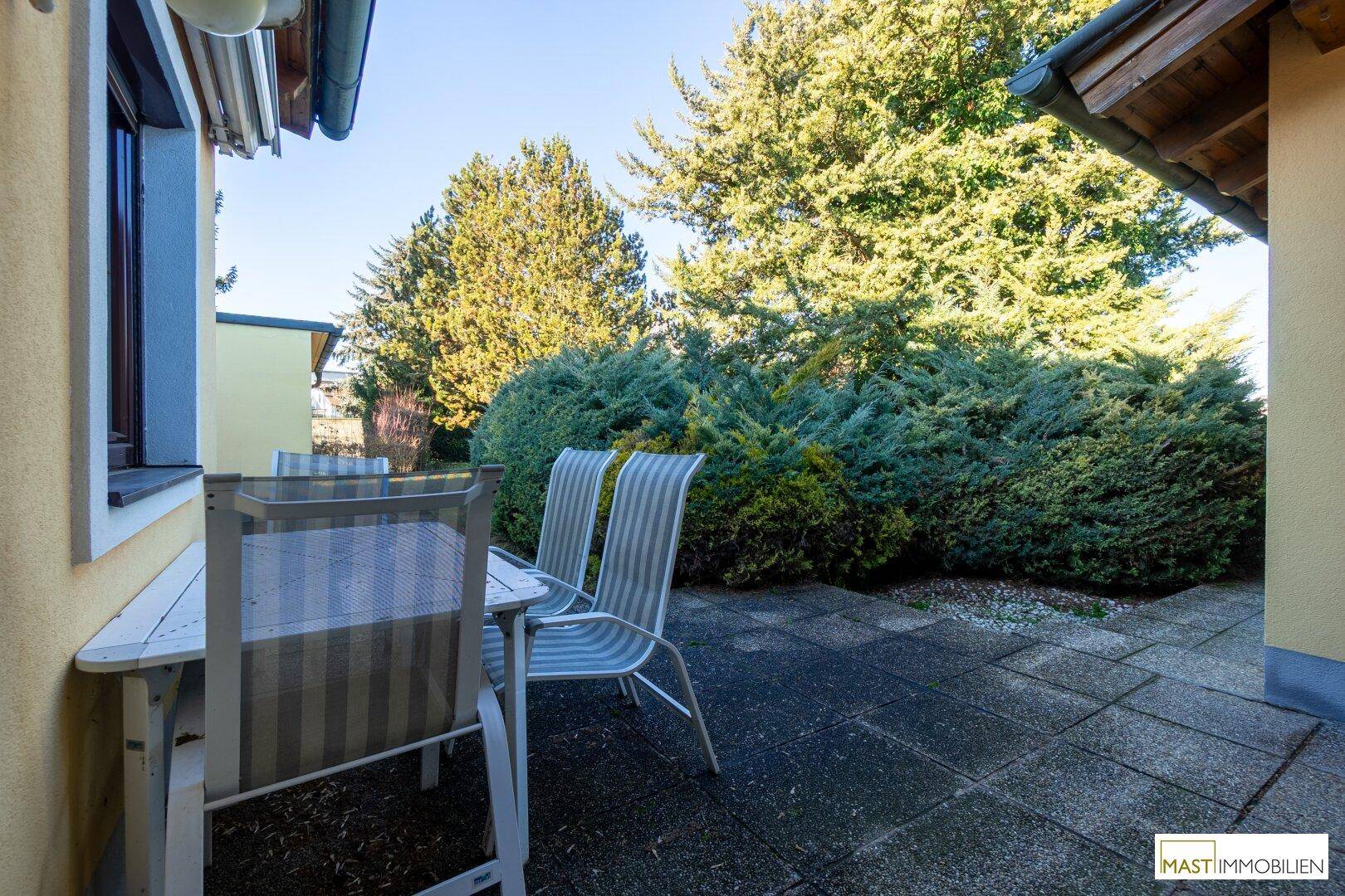 Sonnige Terrasse mit Gartenmöbeln und üppiger Bepflanzung.