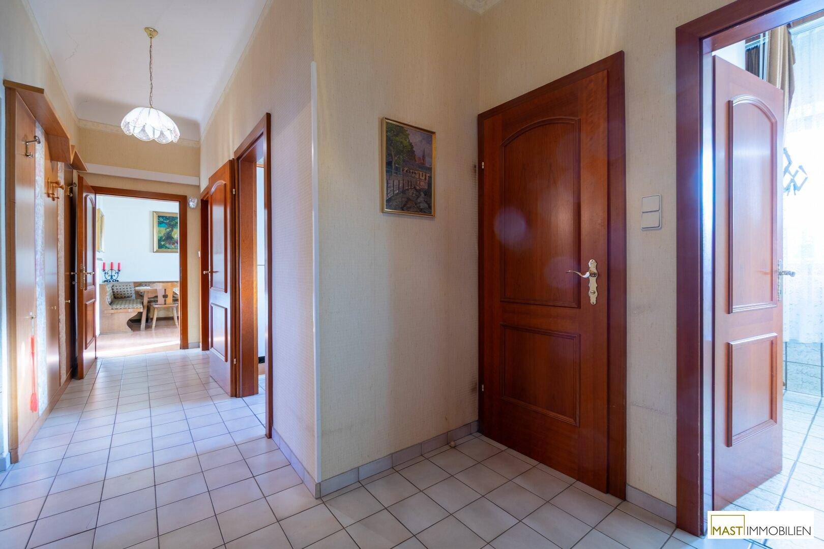 Langer Flur mit Fliesenboden, Holztüren und Zugang zu mehreren Räumen.