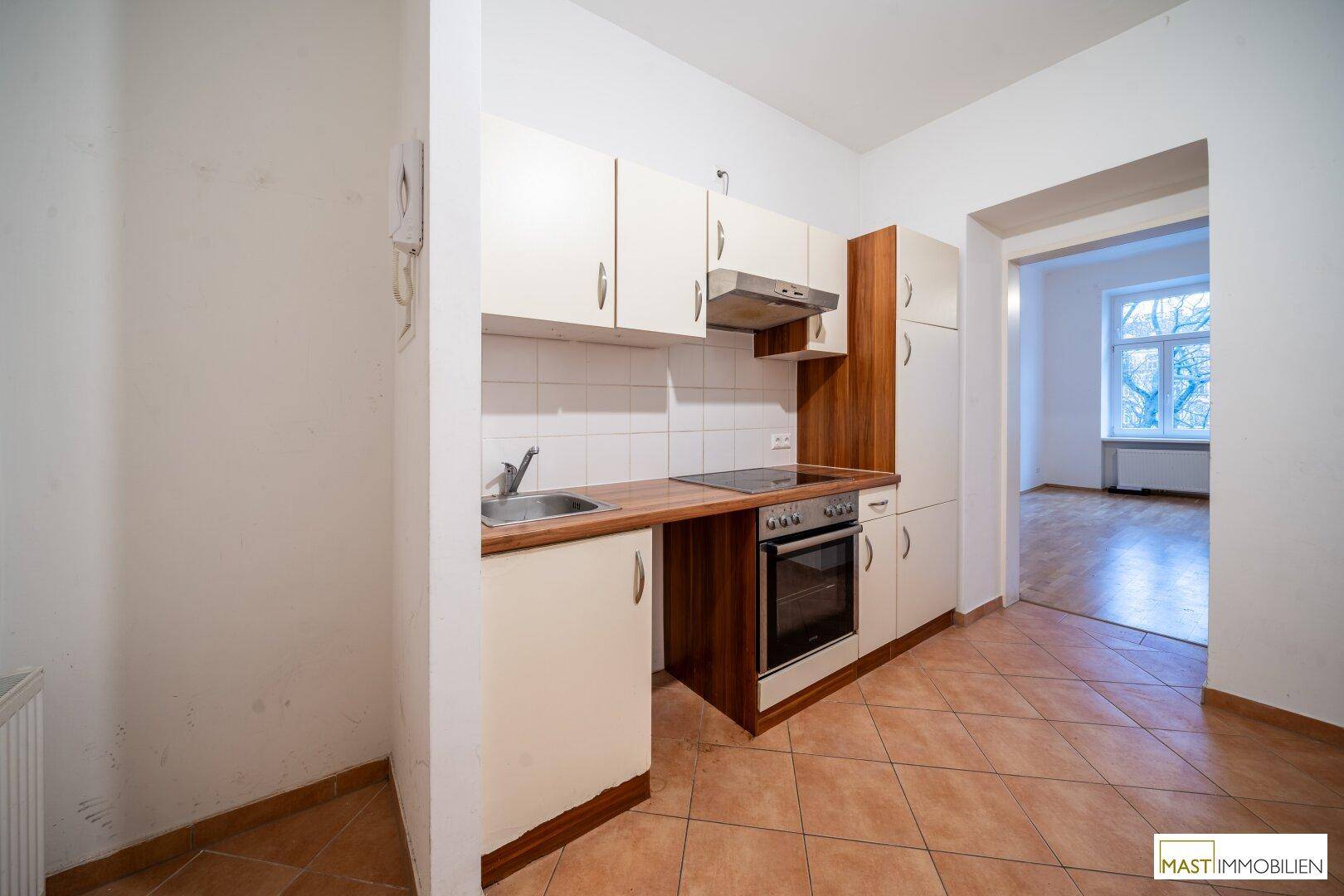 Funktionale Küchenzeile mit hellen Schränken, Fliesenboden und Blick in den Nebenraum.