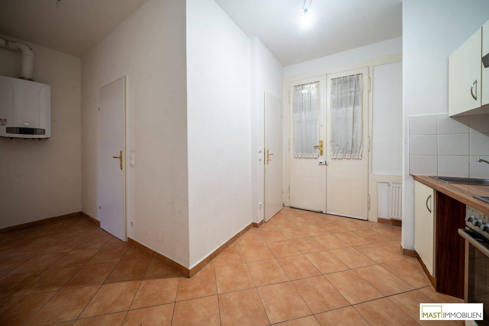 Küchenbereich mit Fliesenboden, weißen Schränken und einem Wandheizkessel.