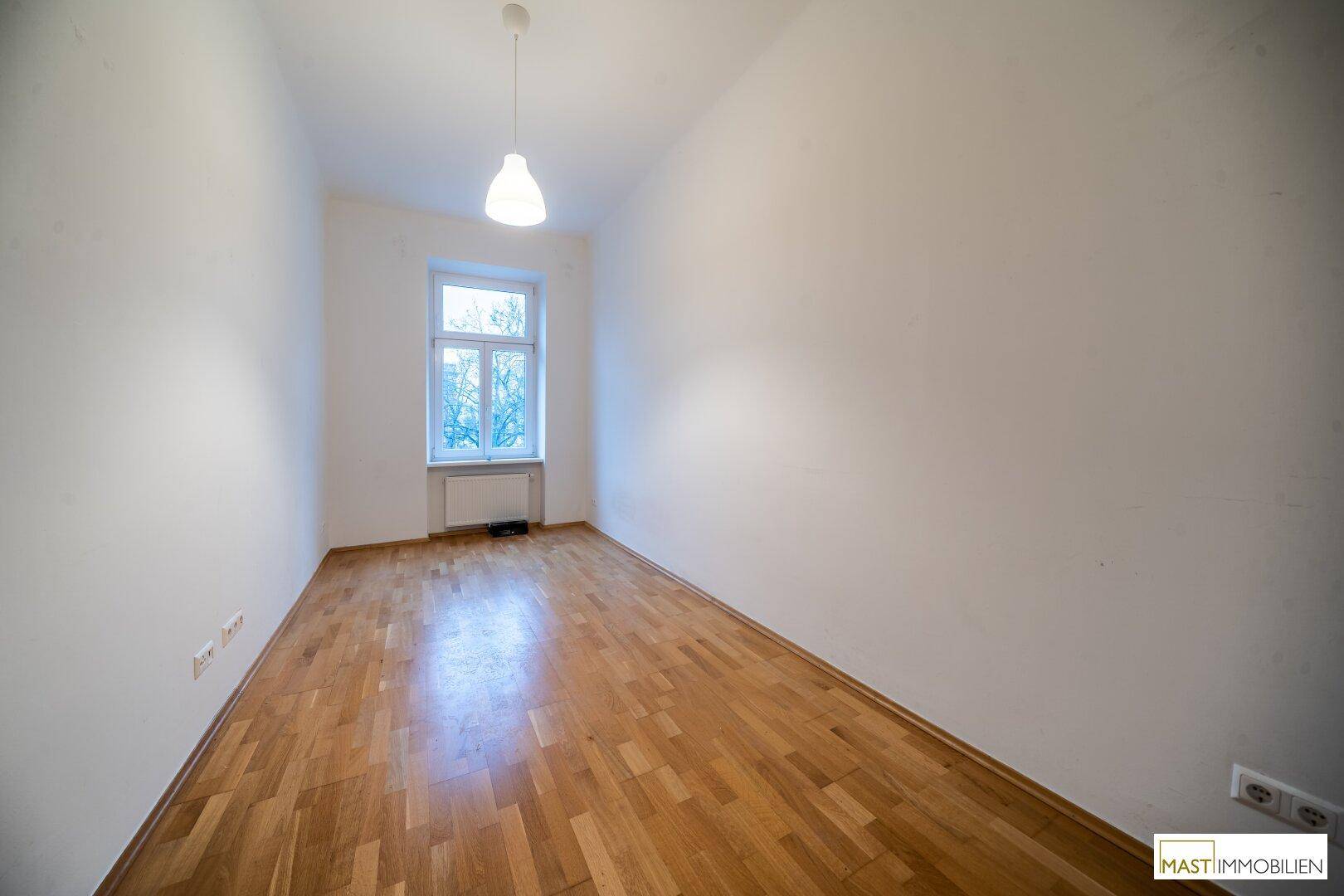 Helles Zimmer mit Parkettboden und einem Fenster, ideal als Schlaf- oder Arbeitszimmer.