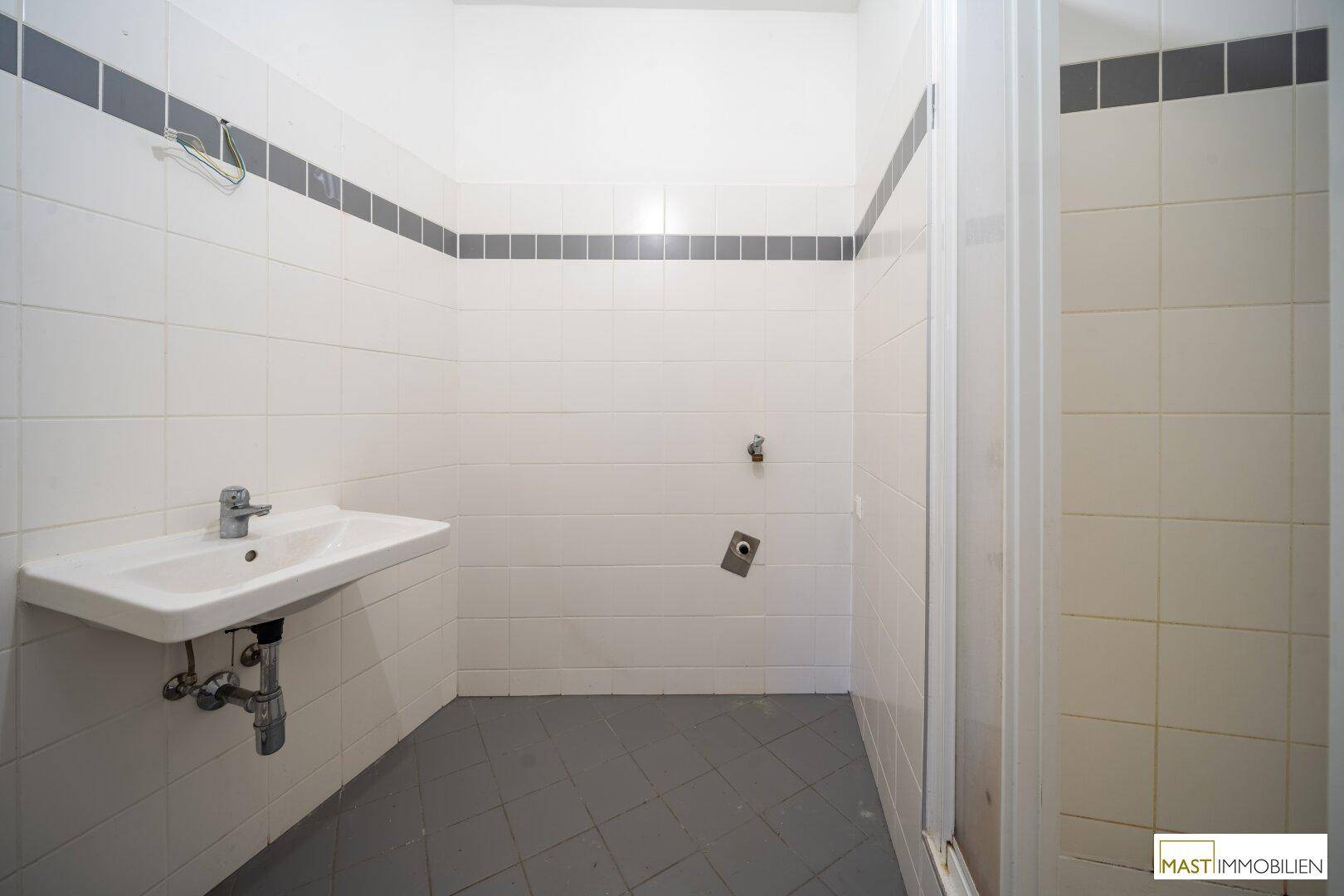 Badezimmer mit weißen Wandfliesen, grauem Boden und einer Duschkabine.