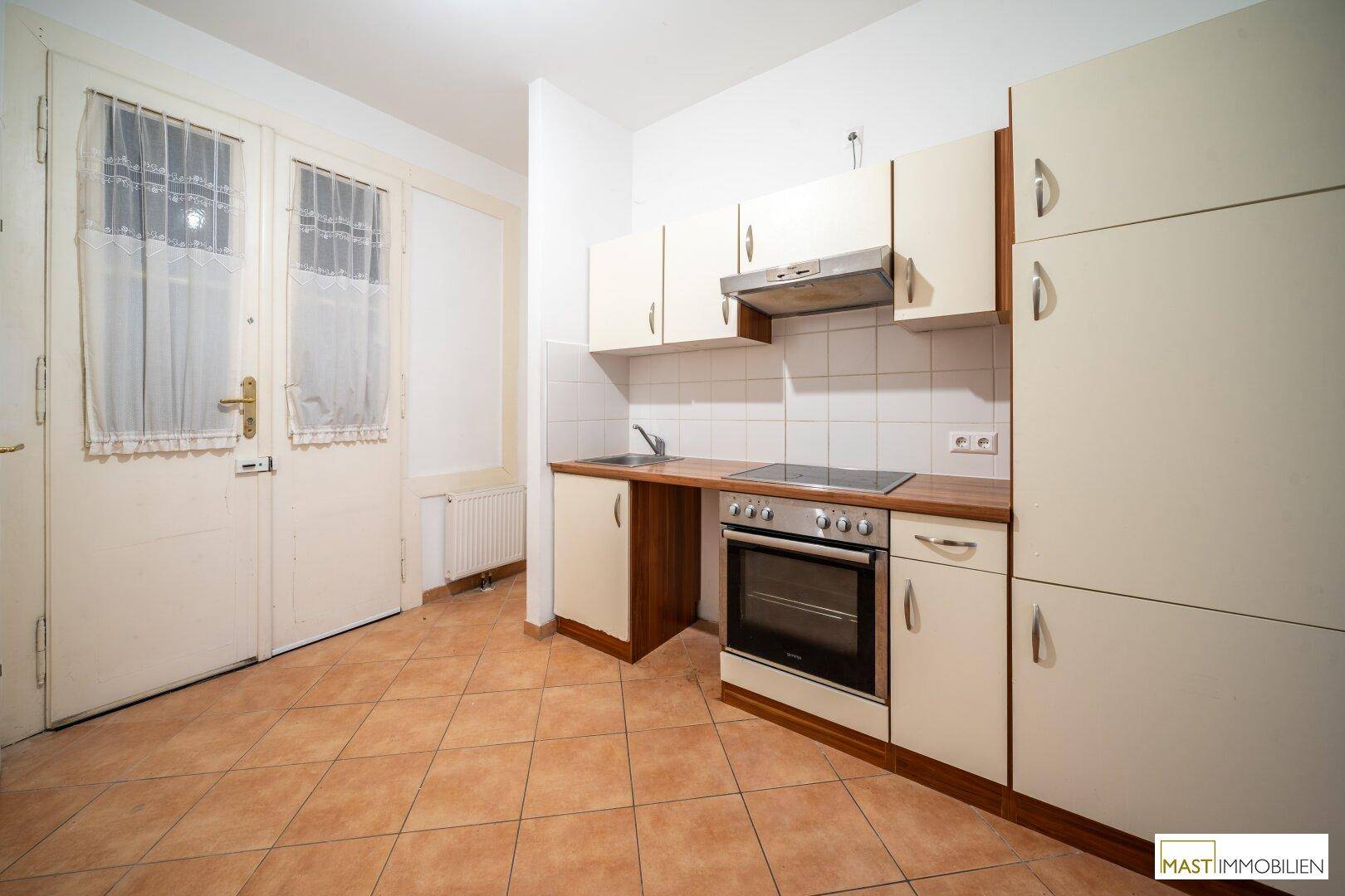 Kompakte Küche mit Fliesenboden, Einbaugeräten und Zugang zu weiteren Räumen.