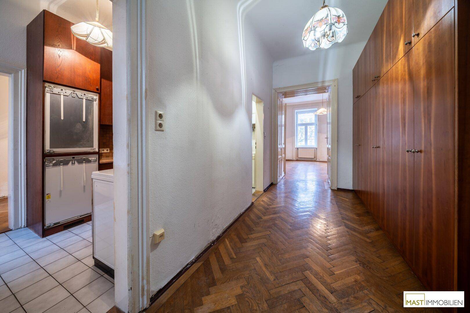 Langer Flur mit Einbauschränken, Fischgrätparkett und Zugang zur Küche.