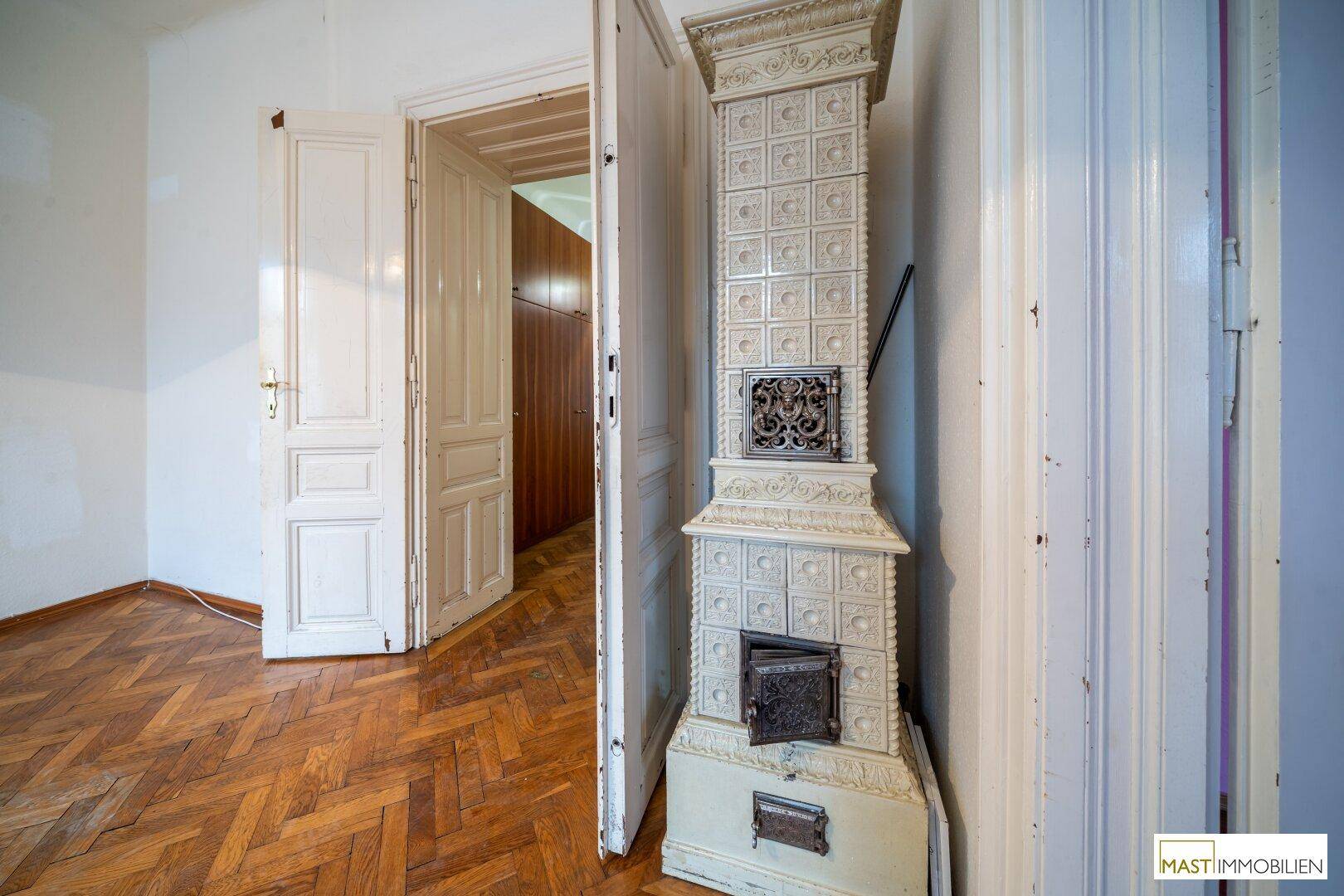 Zimmer mit traditionellem Kachelofen, Fischgrätparkett und hohen weißen Türen.