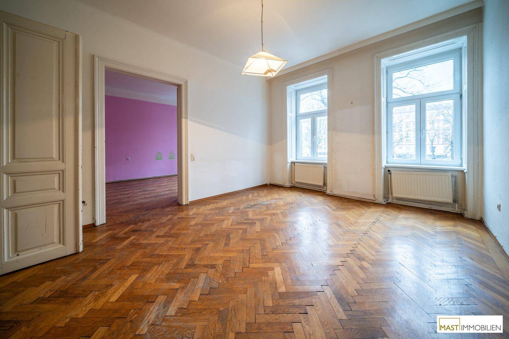 Helles Wohnzimmer mit Fischgrätparkett und Blick in ein angrenzendes, farbiges Zimmer.