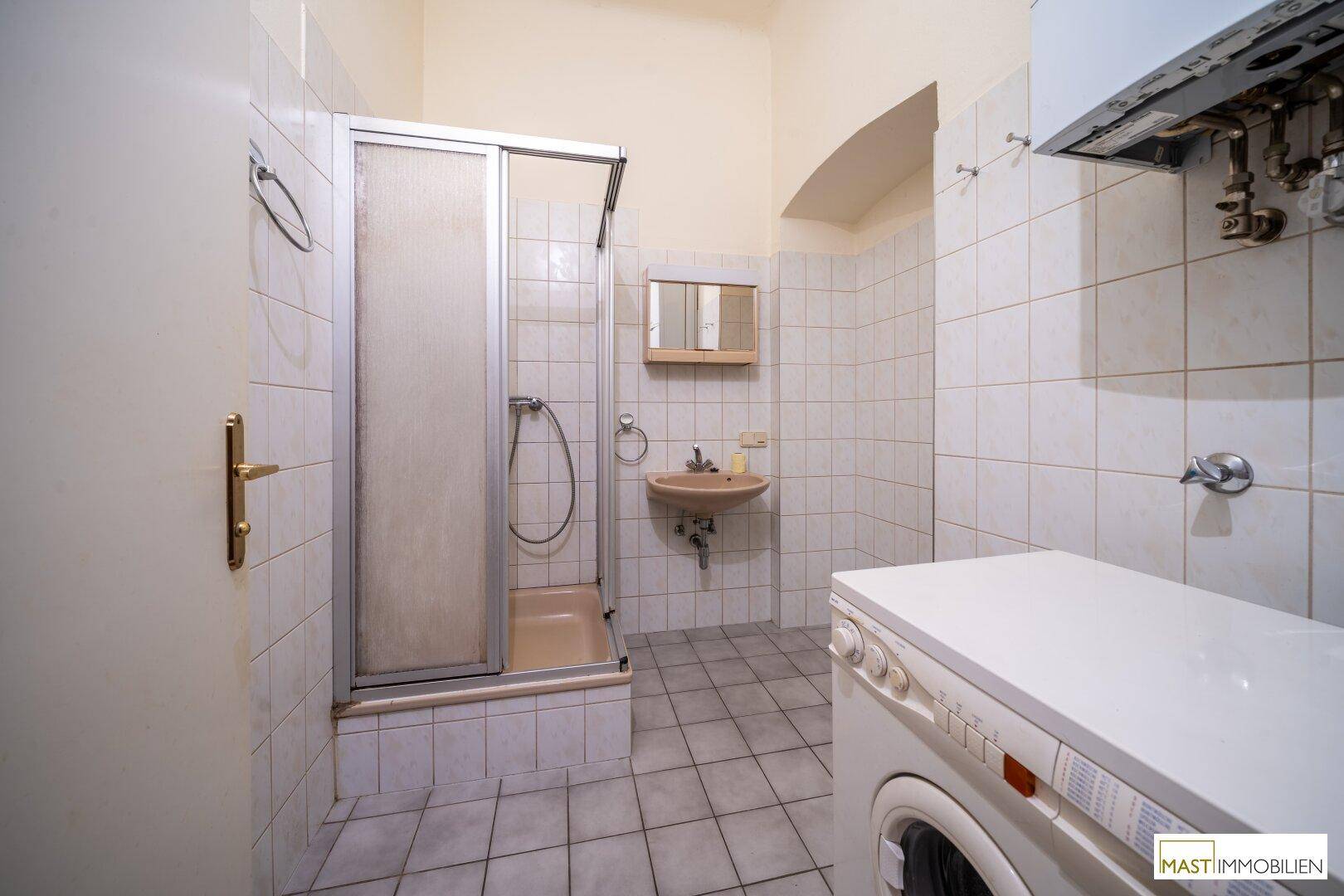 Badezimmer mit Duschkabine, Waschbecken, Waschmaschine und hellen Fliesen.