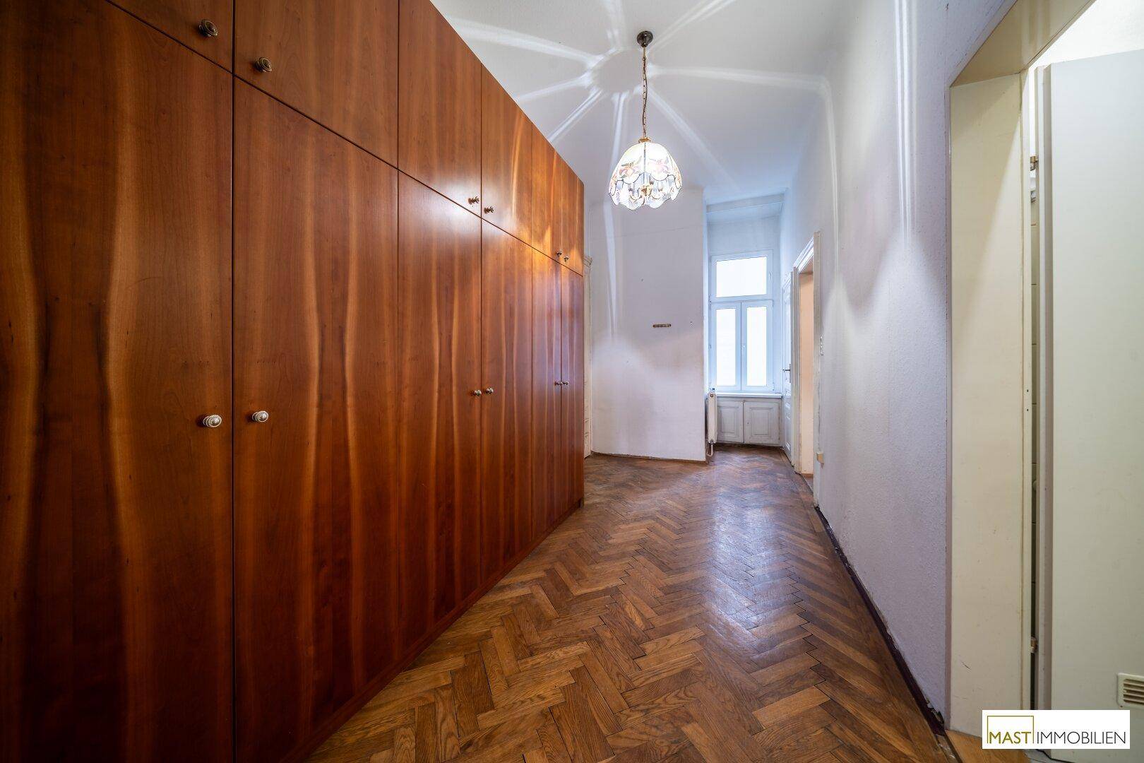 Langer Flur mit hohen Einbauschränken, Fischgrätparkett und Deckenleuchte.