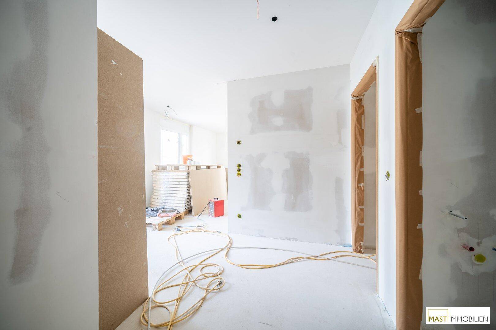 Unfertiger Innenraum mit verputzten Wänden und Elektrokabeln, bereit für den weiteren Ausbau.