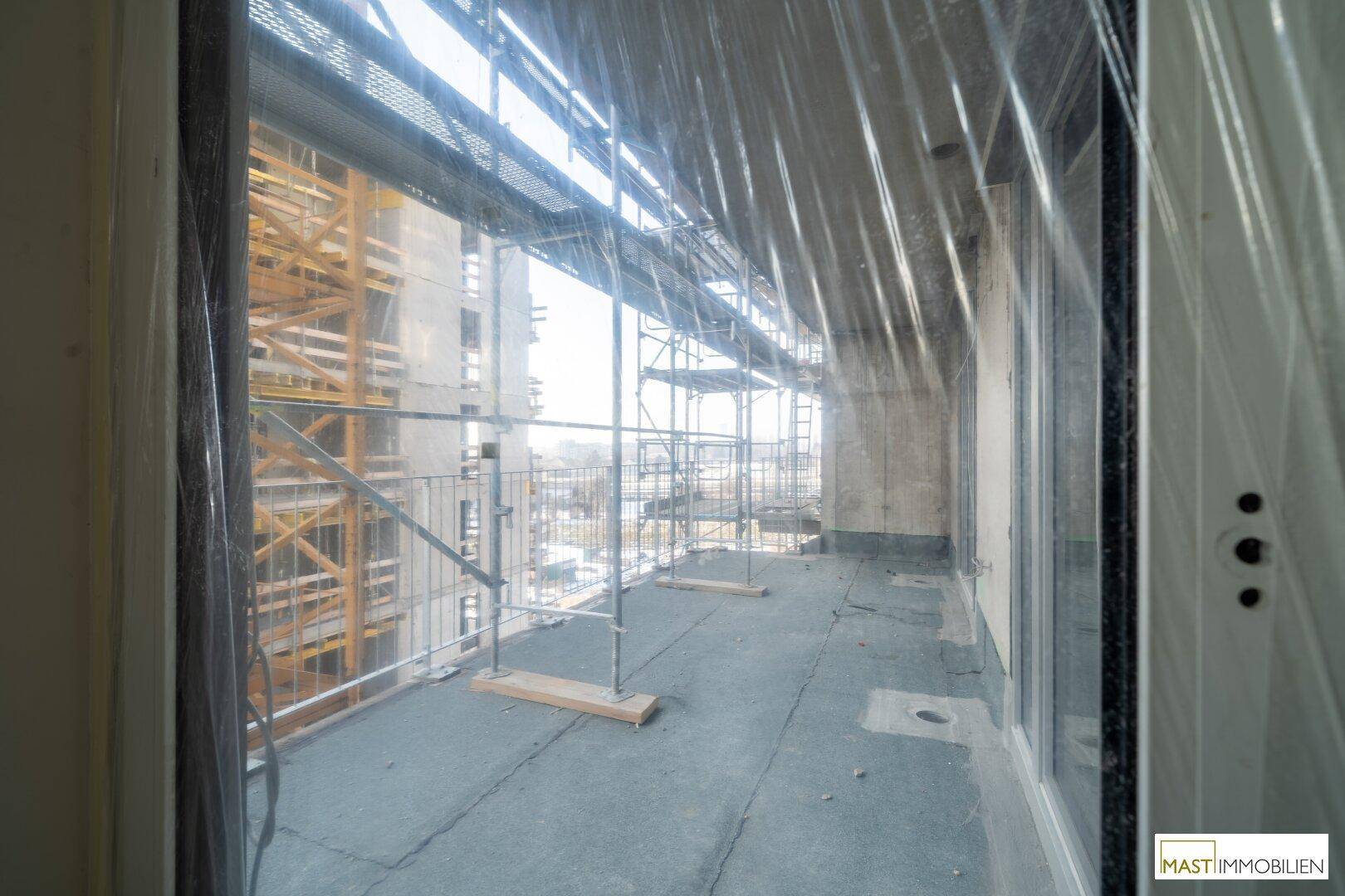 Unfertiger Balkon mit Baugerüst und Schutzfolie, bietet einen Blick auf die umliegende Baustelle.