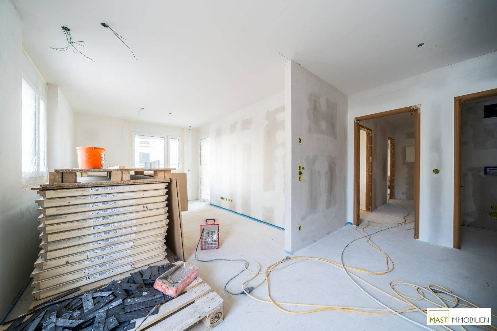 Unfertiger Innenraum mit Baumaterialien, Elektrokabeln und Blick auf die umliegende Baustelle.