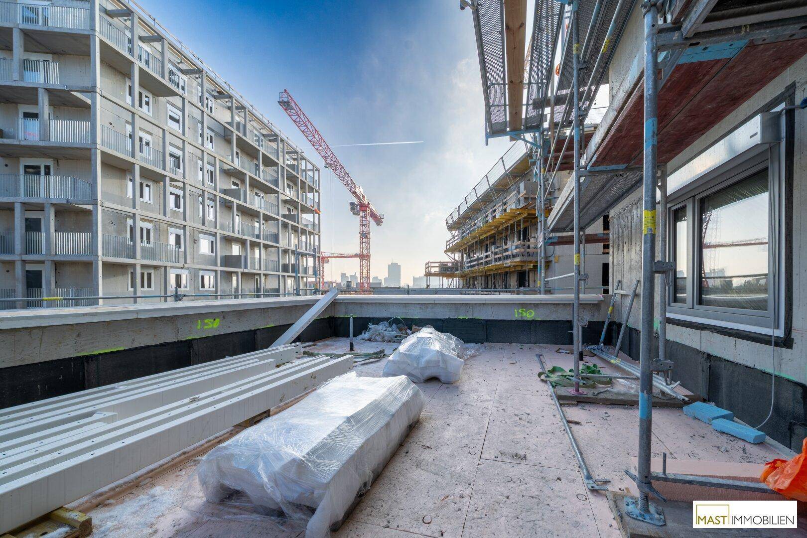 Baustelle mit mehreren Gebäuden, Kränen und Gerüsten unter blauem Himmel.