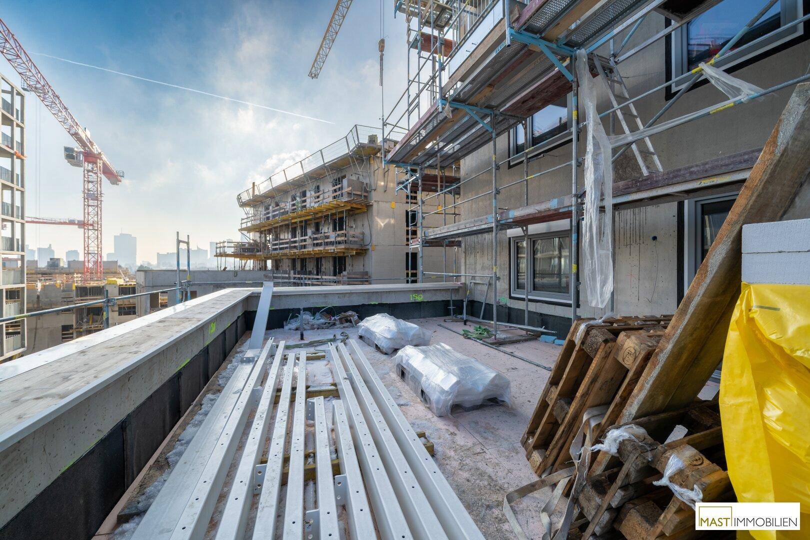 Baustellenansicht mit Kränen, Gerüsten und Baumaterialien auf dem Dach eines neuen Gebäudes.