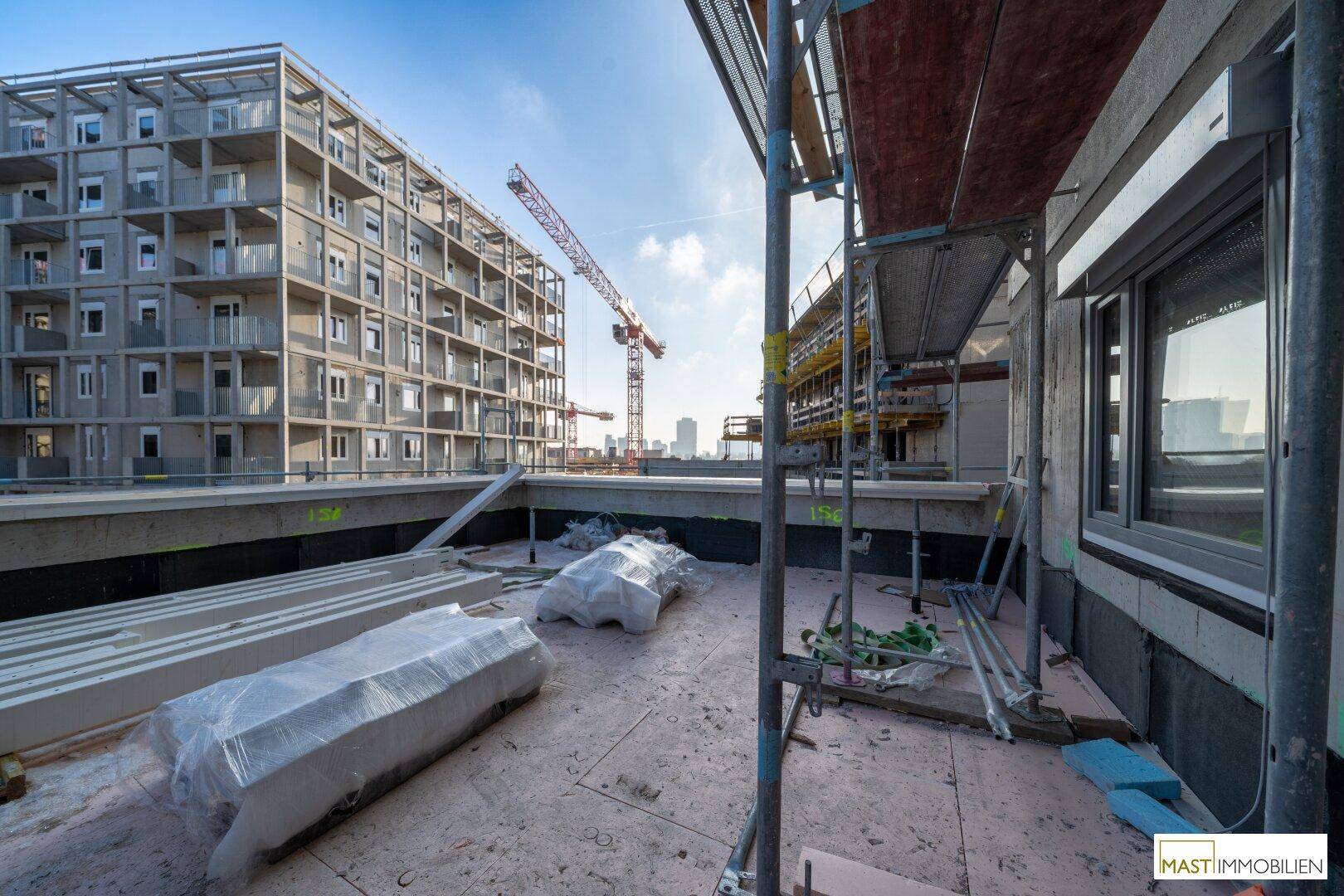 Weitläufige Baustelle mit modernen Gebäuden, Kränen und Baumaterialien unter klarem Himmel.
