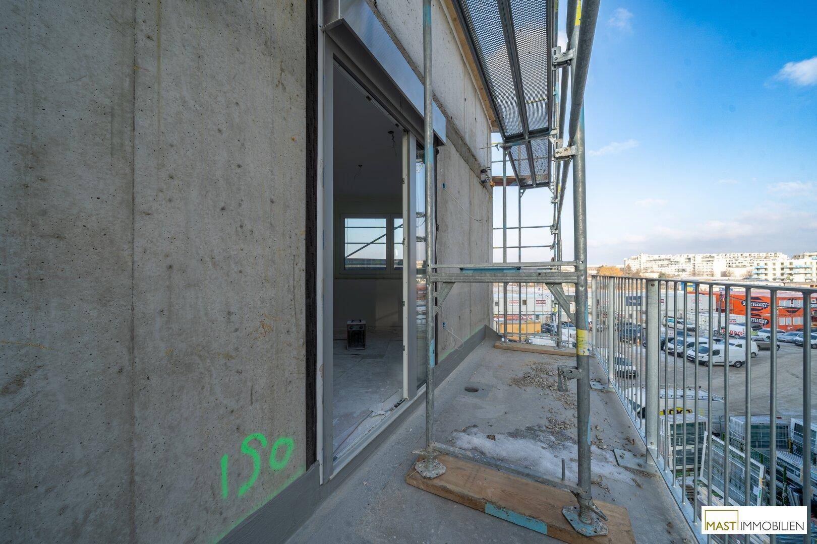 Balkon im Rohbau mit Schiebetür zum Innenraum und Blick auf die Umgebung.