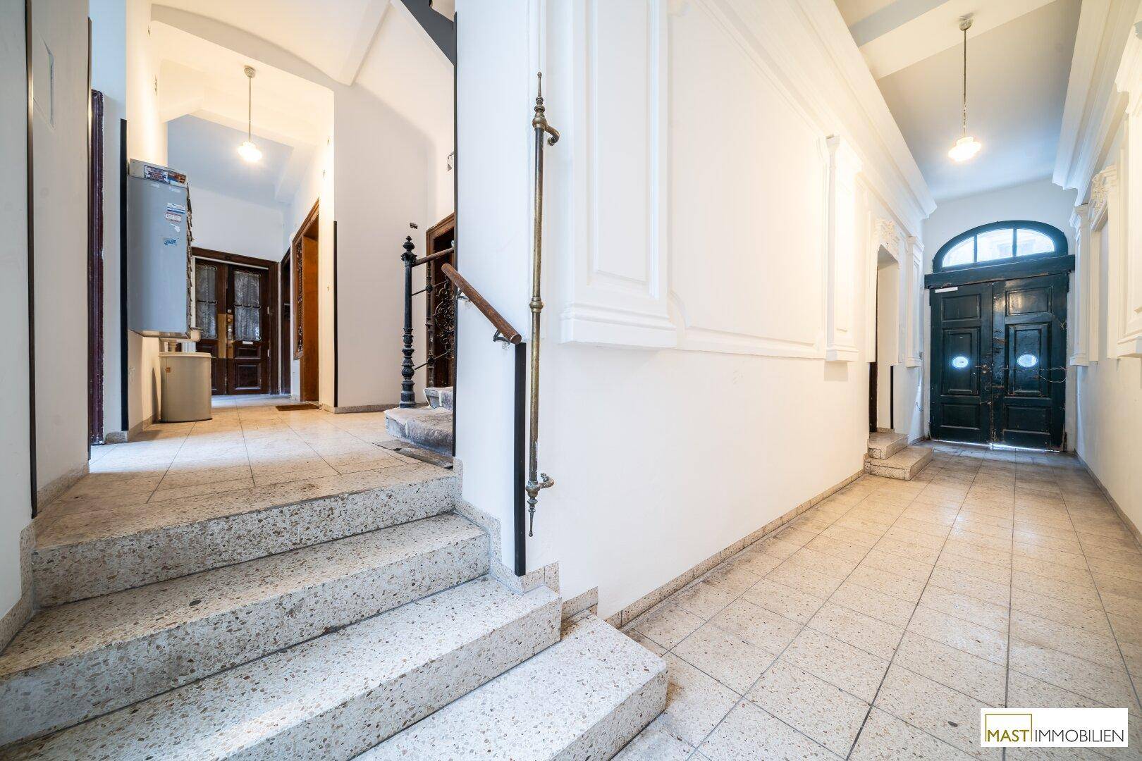 Heller Eingangsbereich mit Steintreppe, Fliesenboden und dekorativem Geländer.